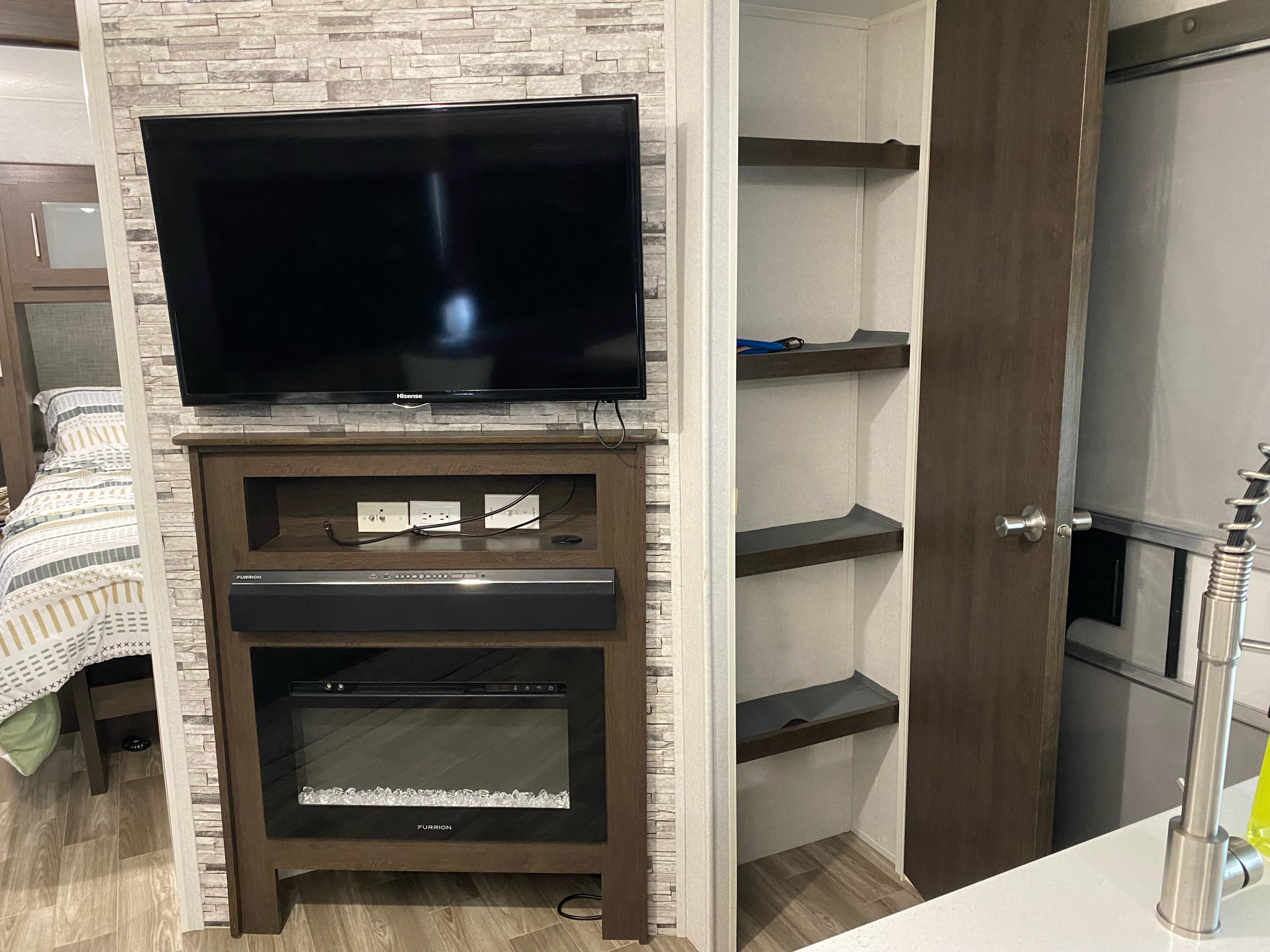 RV rental's inviting interior: bed, entertainment unit with TV, soundbar, electric fireplace, and convenient storage shelves for your trip.. Forest River Wildwood 2020