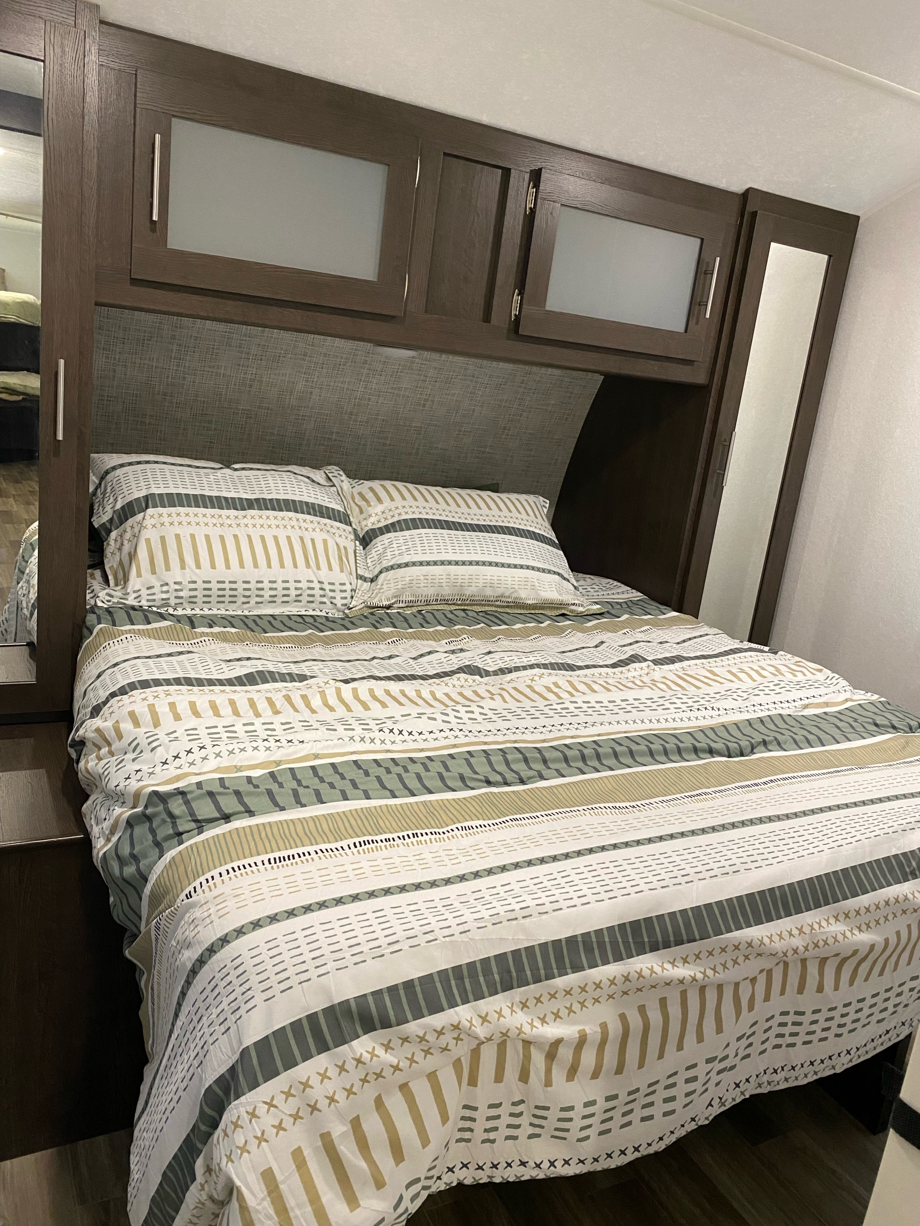 RV rental bedroom: modern decor, striped bedding, overhead storage, textured headboard & mirrored accents.. Forest River Wildwood 2020