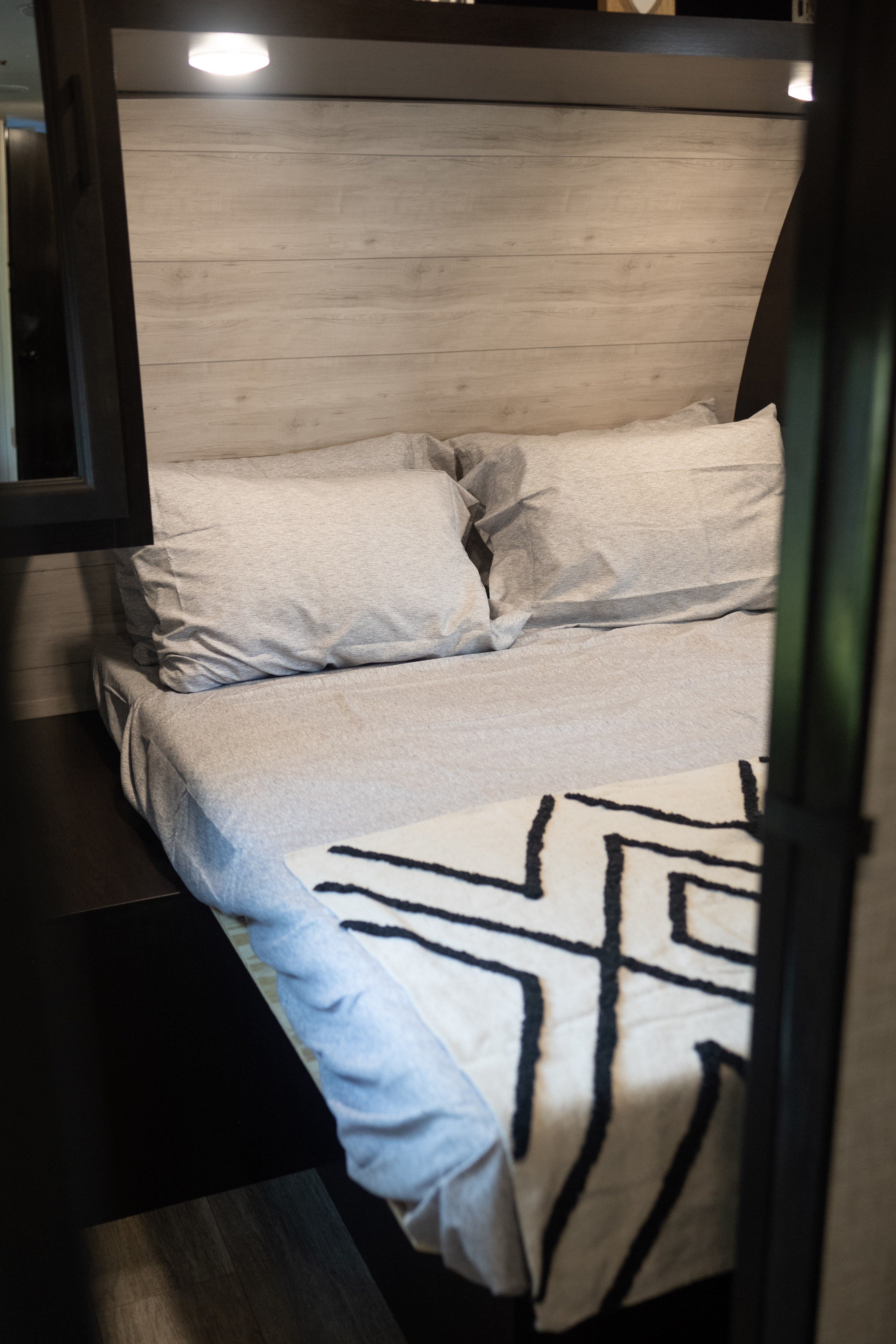 Cozy RV rental bedroom featuring a comfortable bed with light grey bedding, wood paneling, and a stylish geometric throw.. Jayco Jay Flight 2023
