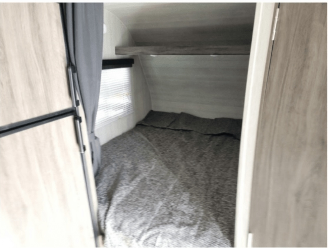 RV rental bedroom interior: A cozy bed with gray bedding, a small window, and an overhead shelf. Compact RV living space.. Genesis Supreme Rv Powerlite Prime 1915 2022