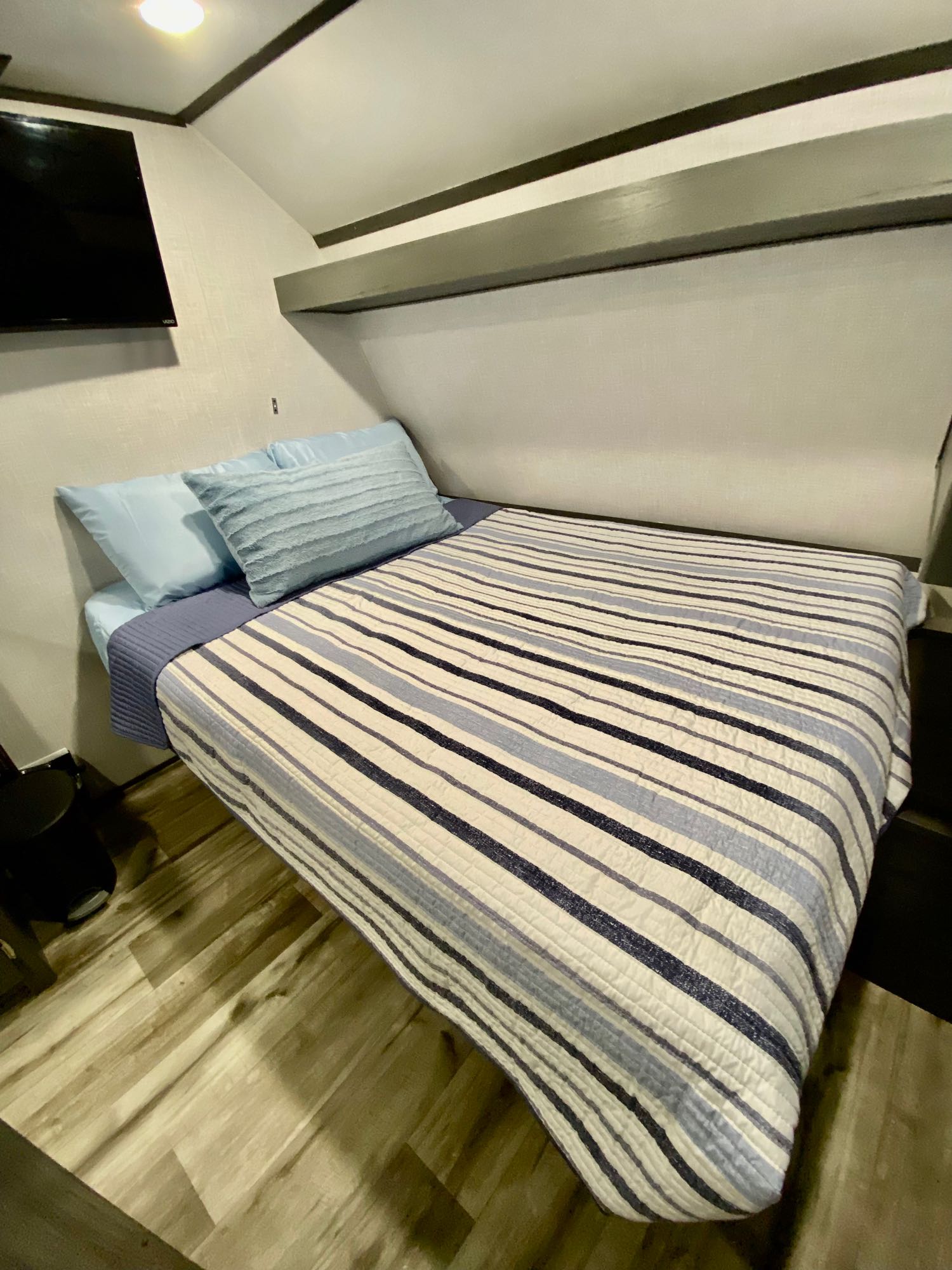 Cozy RV rental bedroom: light blue bedding, striped comforter, and mounted TV for comfortable sleeping.. Aspen Trail LE 2022