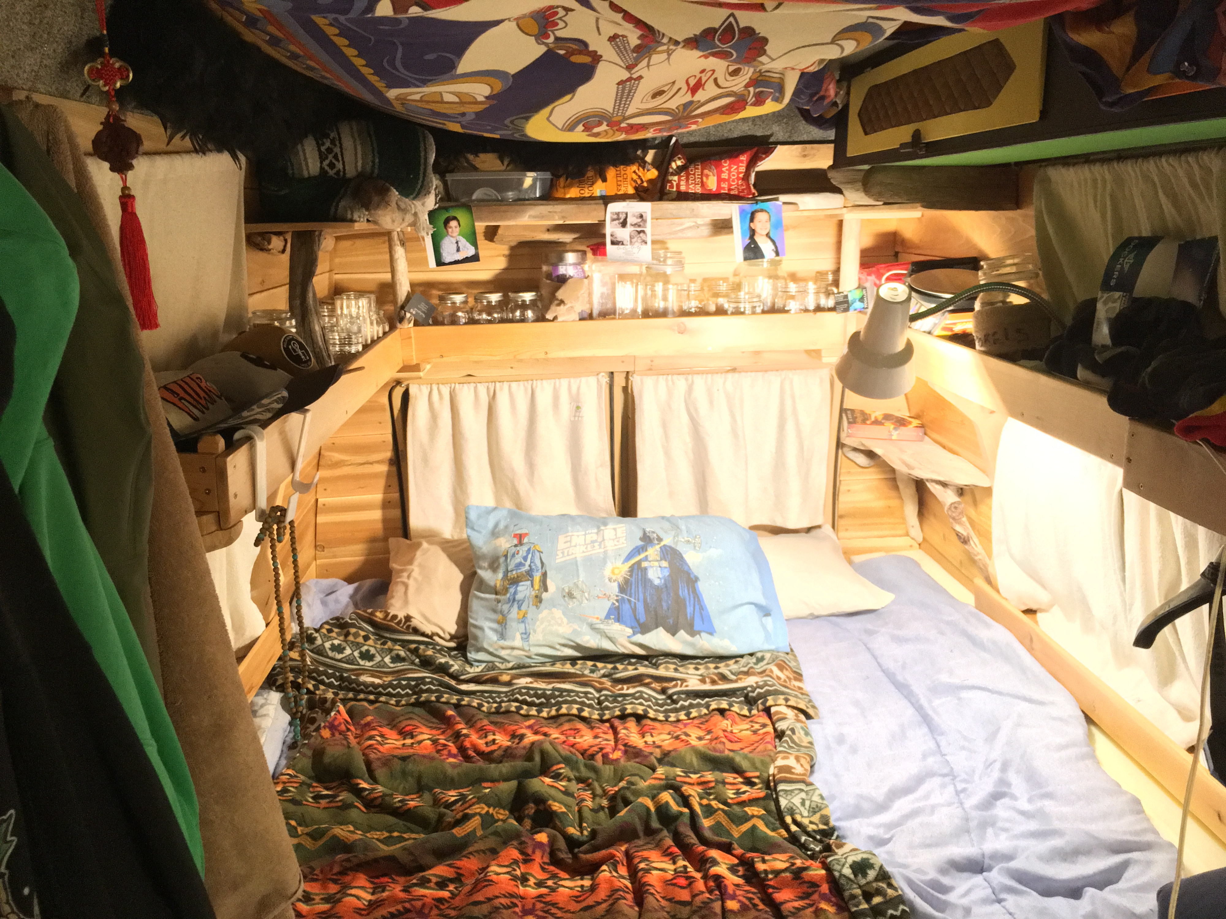 Cozy RV rental interior with a bed, wood paneling, and personal decor, perfect for compact living.. Dodge B Van 1977