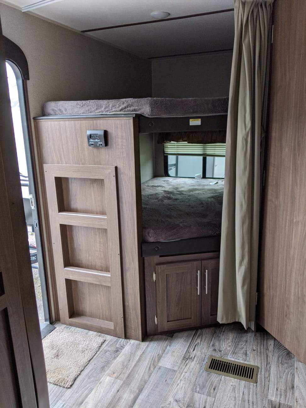 Inside an RV rental: two bunk beds with wood-look decor, a control panel, and privacy curtains.. Keystone RV Hideout Luxury 2021