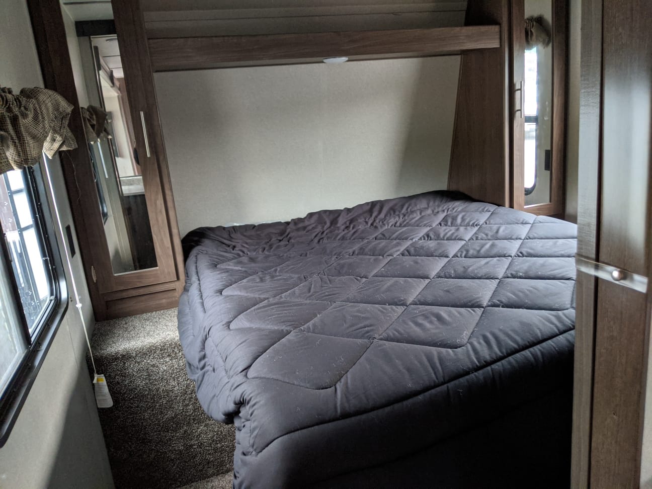Interior of an RV rental bedroom showing a large bed with dark comforter, built-in closet, and window.. Keystone RV Hideout Luxury 2021