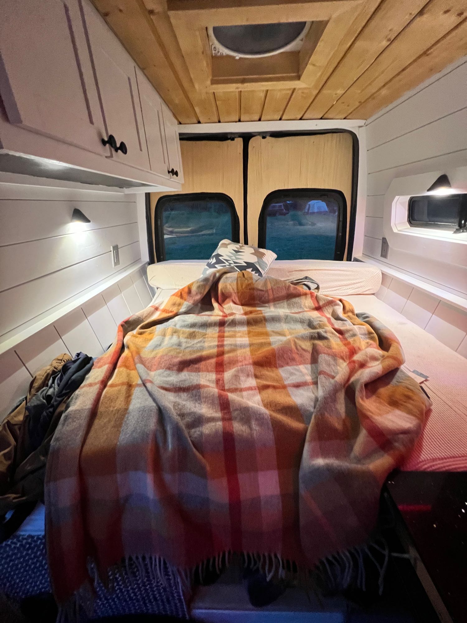 Cozy RV rental interior with bed, plaid blanket, and overhead cabinets. Views out the back windows.. Mercedes-Benz Sprinter RV Motorhome Campervan 2019