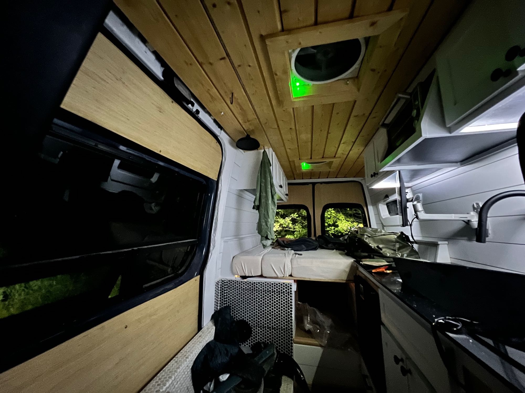 Inside a modern camper van, perfect for RV rental trips. Wooden ceiling, green-lit vents, bed, and kitchen visible.. Mercedes-Benz Sprinter RV Motorhome Campervan 2019