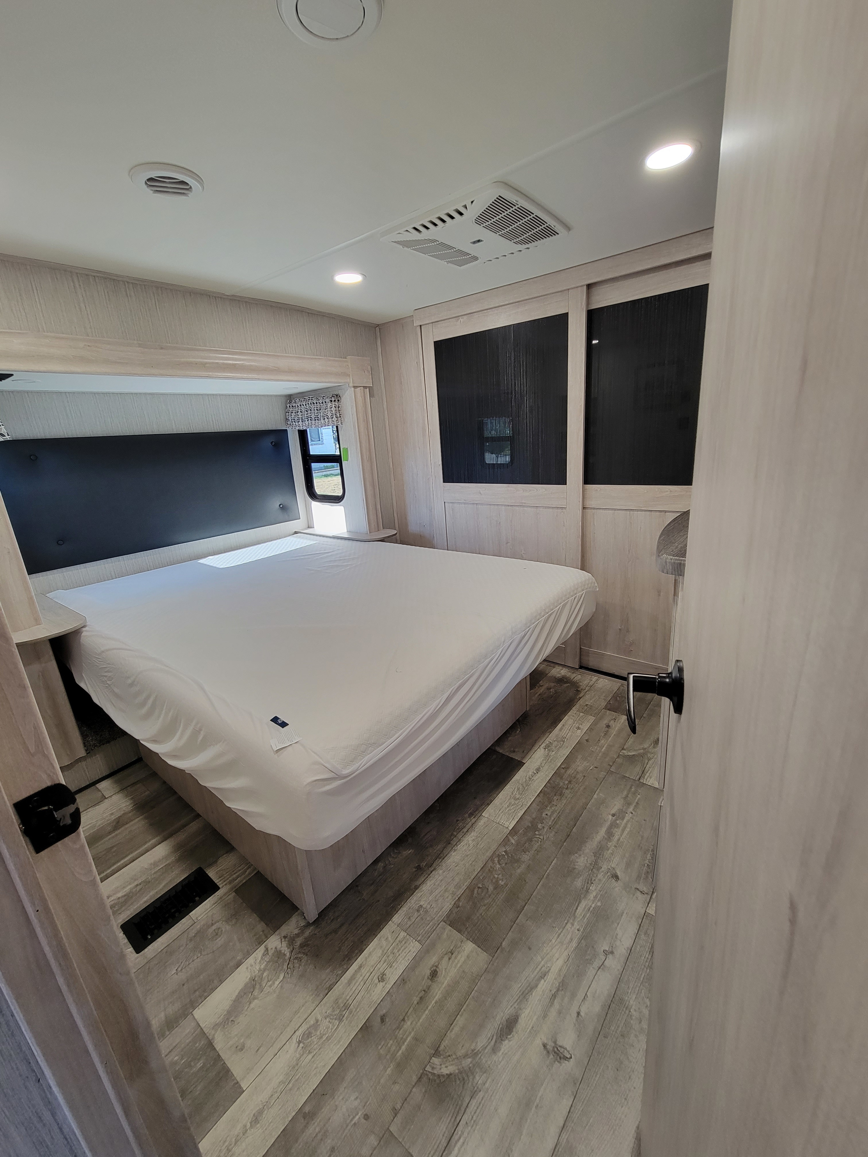 Modern RV rental bedroom: light wood, comfy bed, black headboard, ceiling lights & AC, and sliding closet storage.. Forest River Sandpiper 2022