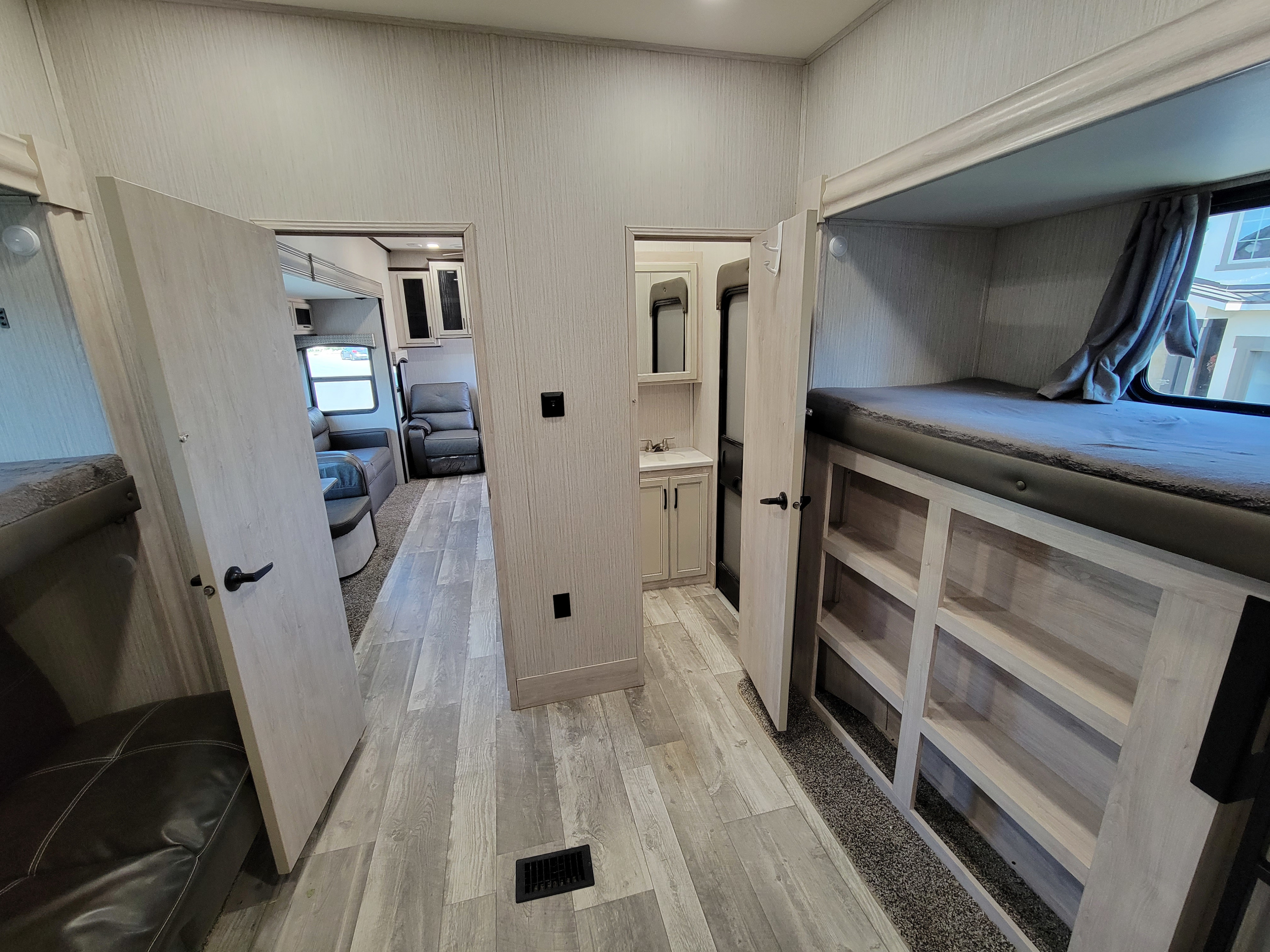 Spacious RV rental interior featuring a hallway, living area, bathroom vanity, and bunk beds with shelving.. Forest River Sandpiper 2022