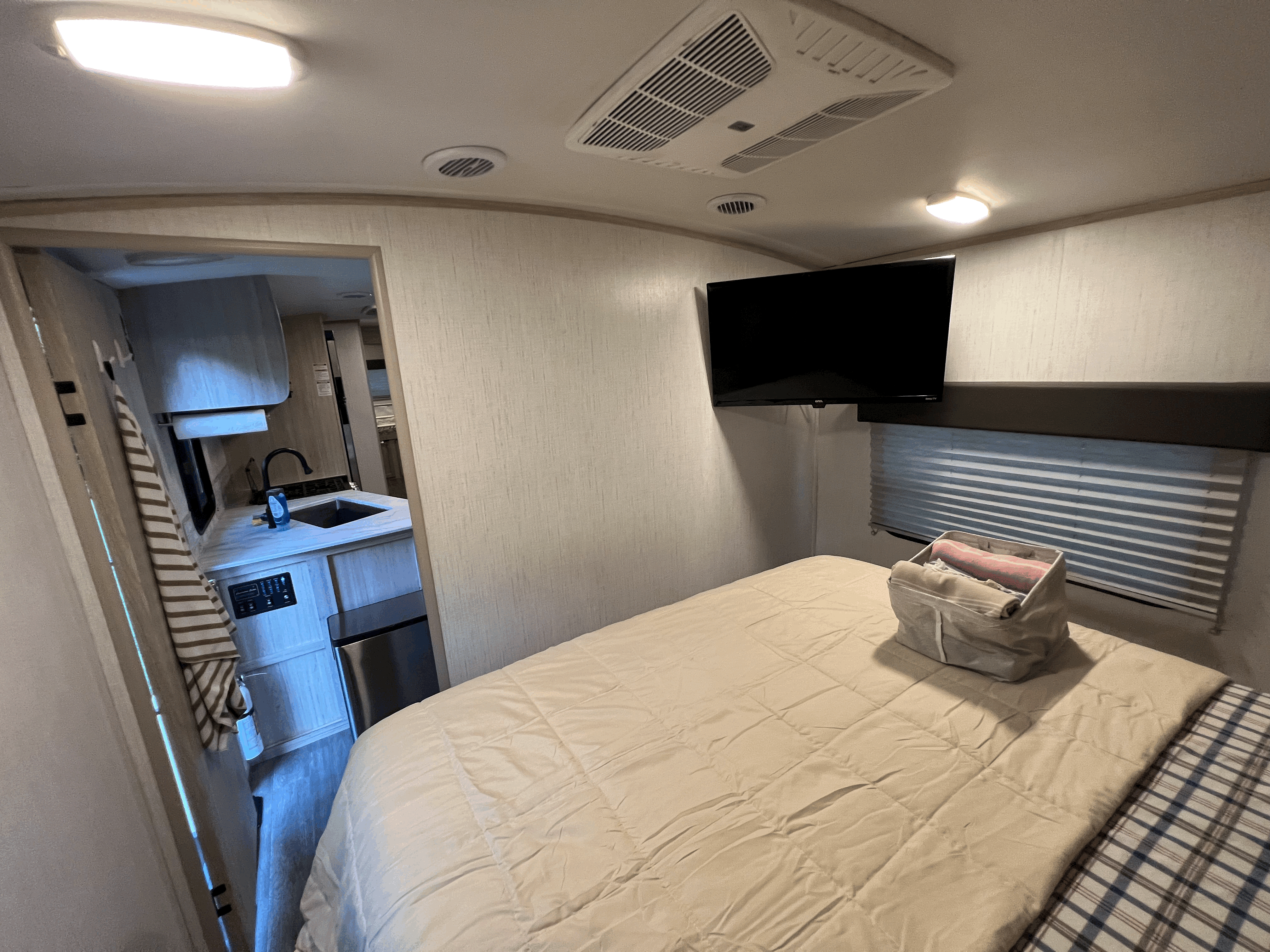 Cozy RV rental interior featuring a comfortable bedroom with a mounted TV and a compact kitchen accessible through an archway.. Shadow Trailers shadow cruiser 2022