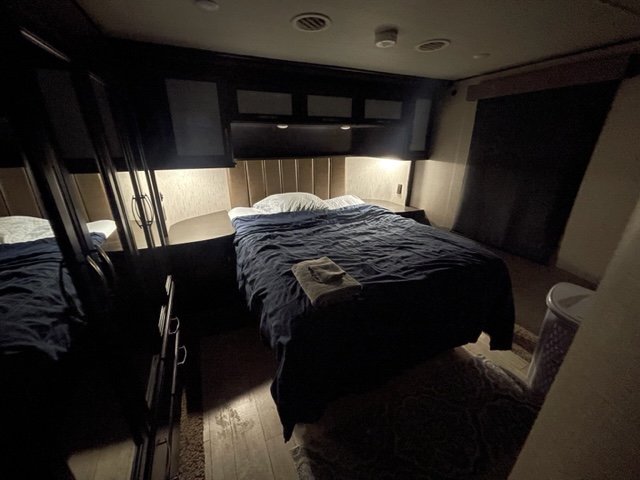 Nighttime view inside a compact rv rental bedroom. A bed with blue bedding and warm light offers a cozy stay.. Grand Design Momentum 2018