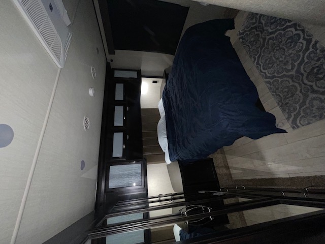 This RV rental shows a well-appointed bedroom interior, featuring a dark blue comforter, patterned rug, and ceiling AC unit.. Grand Design Momentum 2018