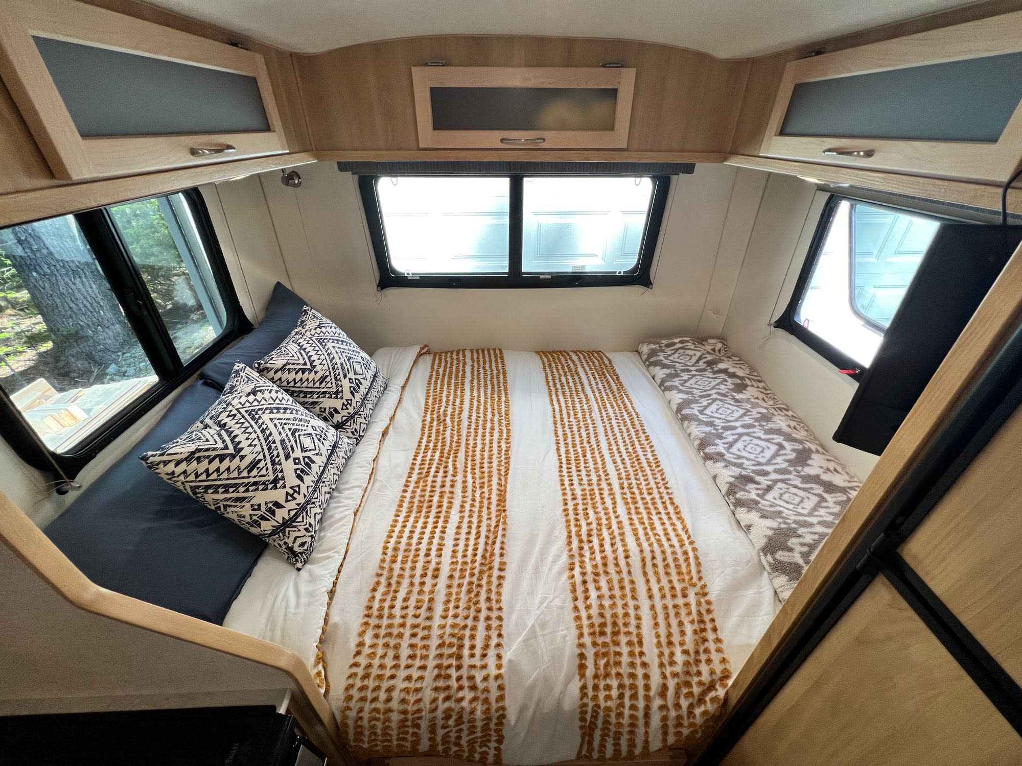 Discover this cozy RV rental's interior! A comfortable bed with patterned bedding, surrounded by windows & overhead storage.. Escape Trailer Escape Trailer Trailer 2022