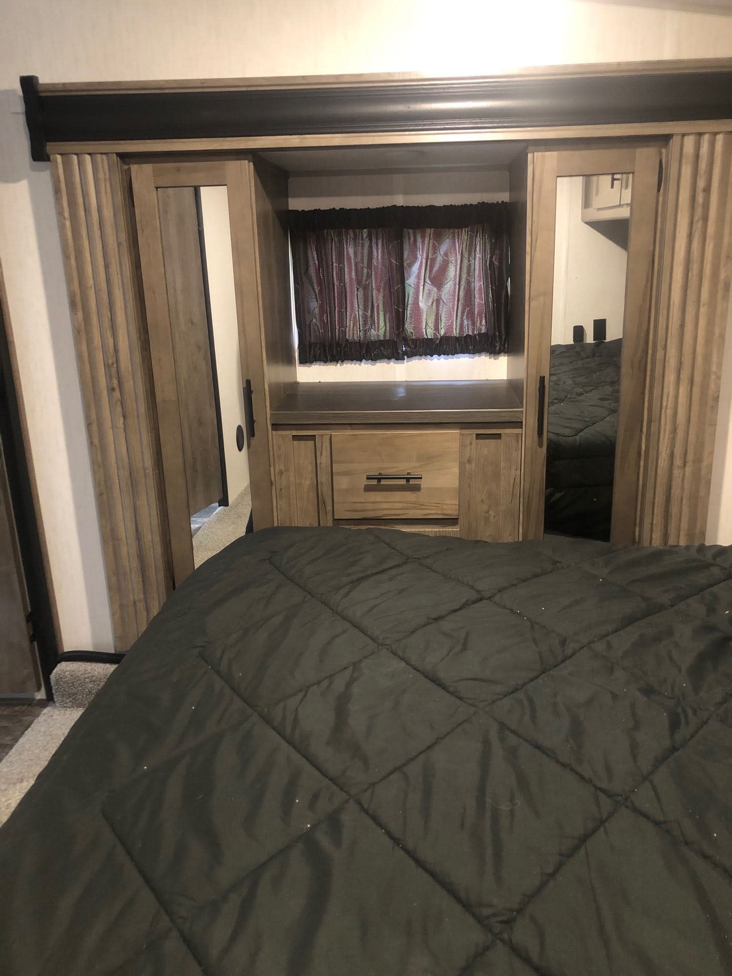 RV rental bedroom: dark quilted comforter on bed, wooden built-in storage with TV niche, and sliding barn doors.. Forest River Cherokee Wolf Pack Toy Hauler 2021