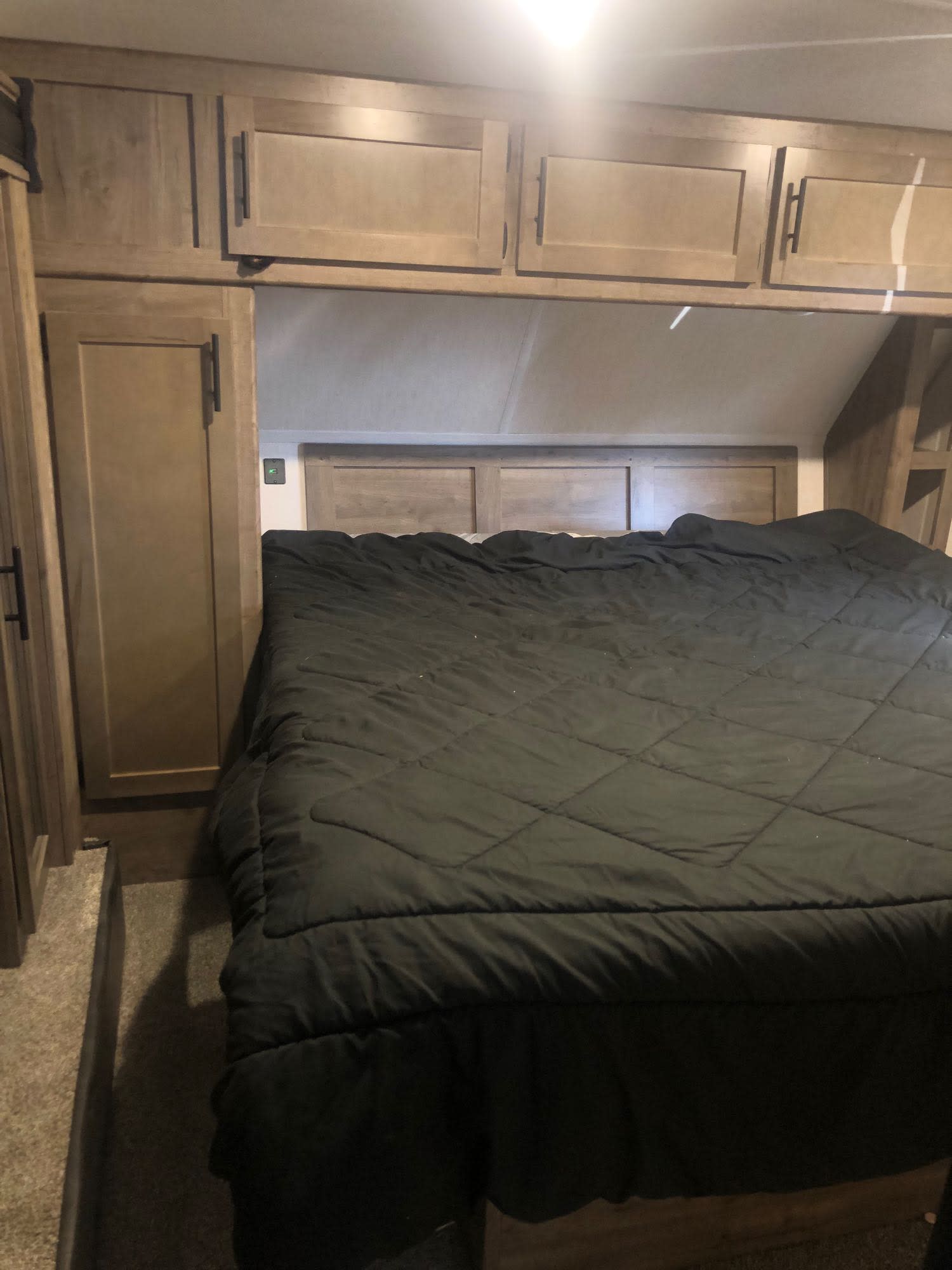 Cozy RV rental bedroom featuring a spacious bed with dark bedding, overhead cabinets, and built-in storage.. Forest River Cherokee Wolf Pack Toy Hauler 2021