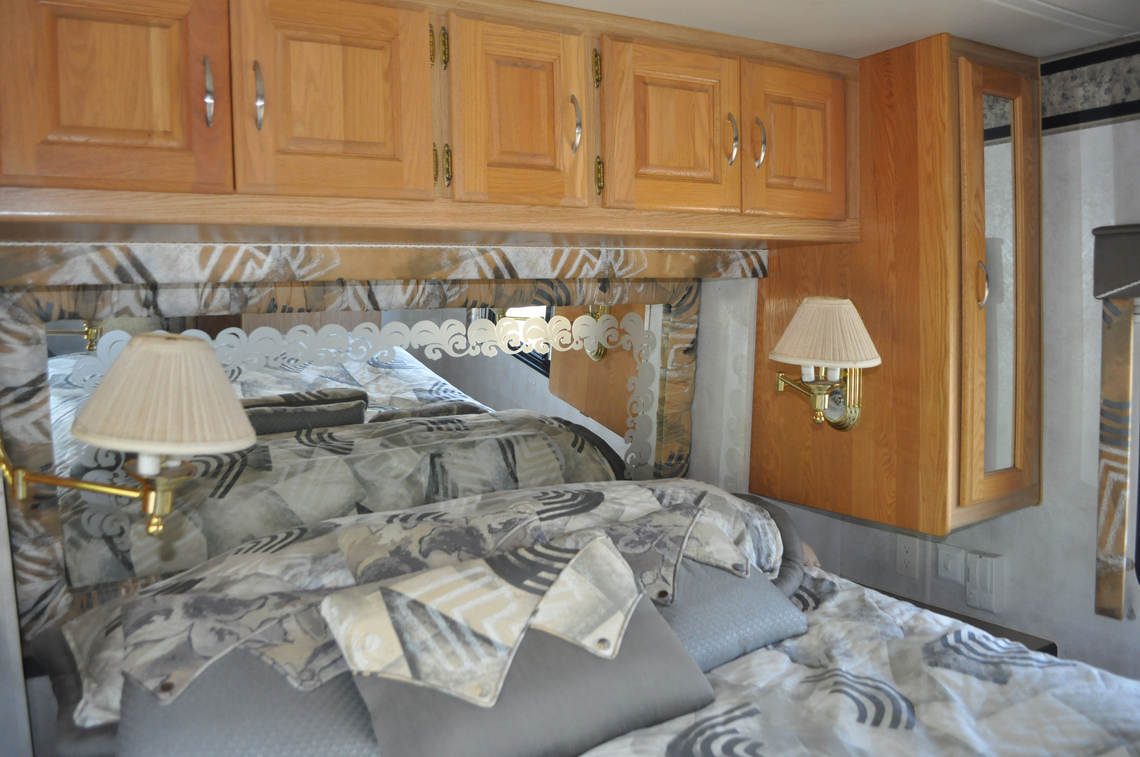 Cozy RV rental bedroom featuring wooden overhead cabinets, a comfortable bed, and soft wall lamps, ideal for travel.. Holiday Rambler Endeavor 2000