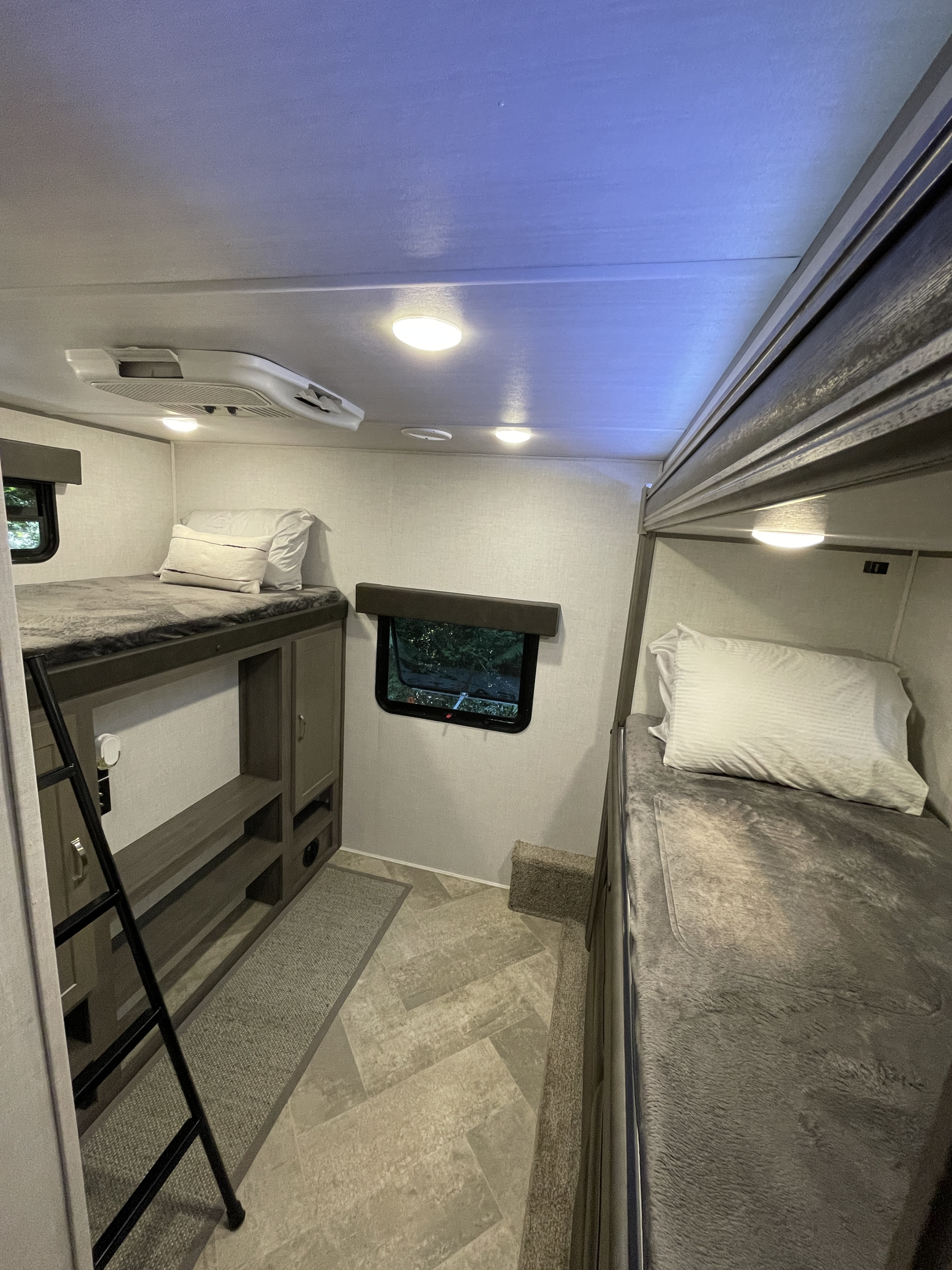 RV rental interior features a compact sleeping area with two bunk beds, ladder, AC, and a window.. East to West Alta 2021