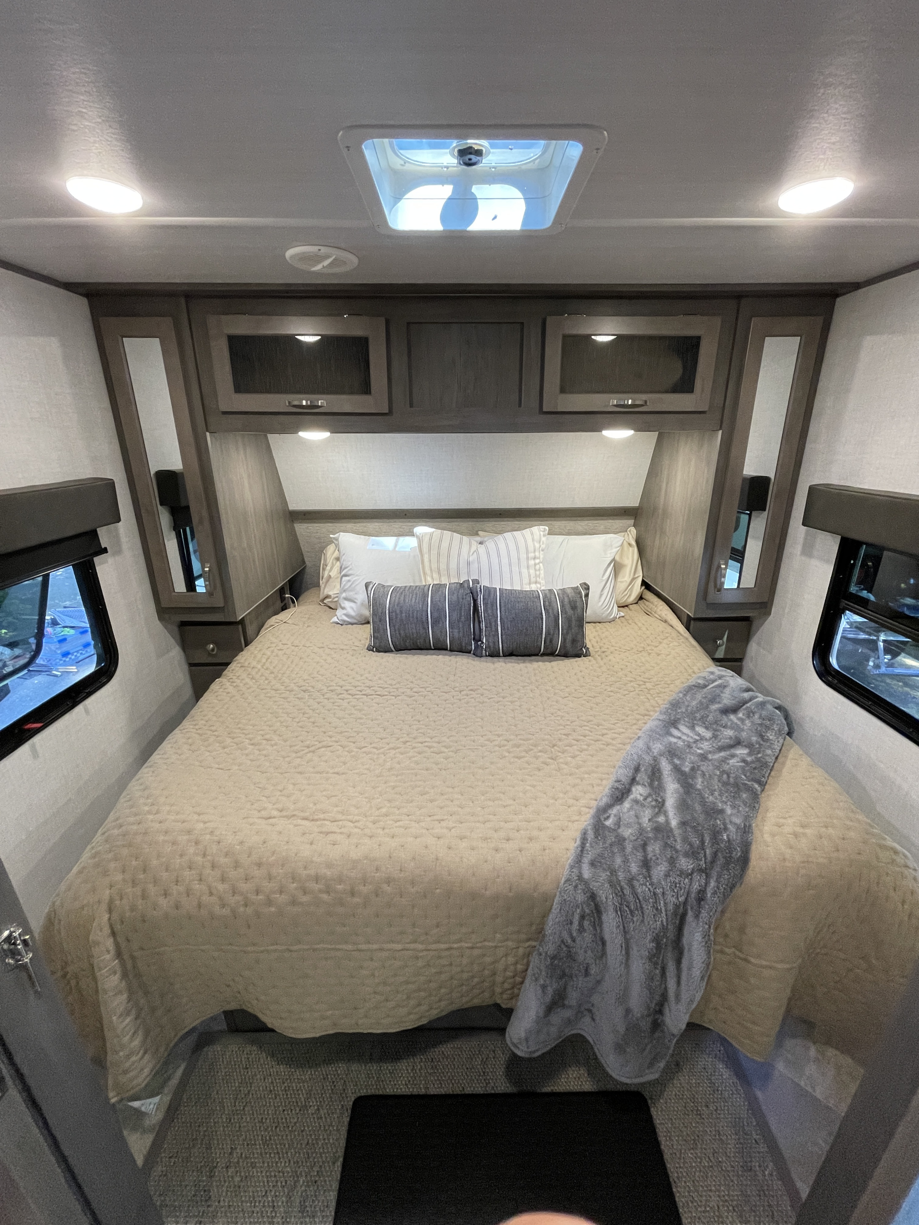 Comfortable RV rental bedroom featuring a large bed with neutral bedding, overhead storage, and bright lighting.. East to West Alta 2021