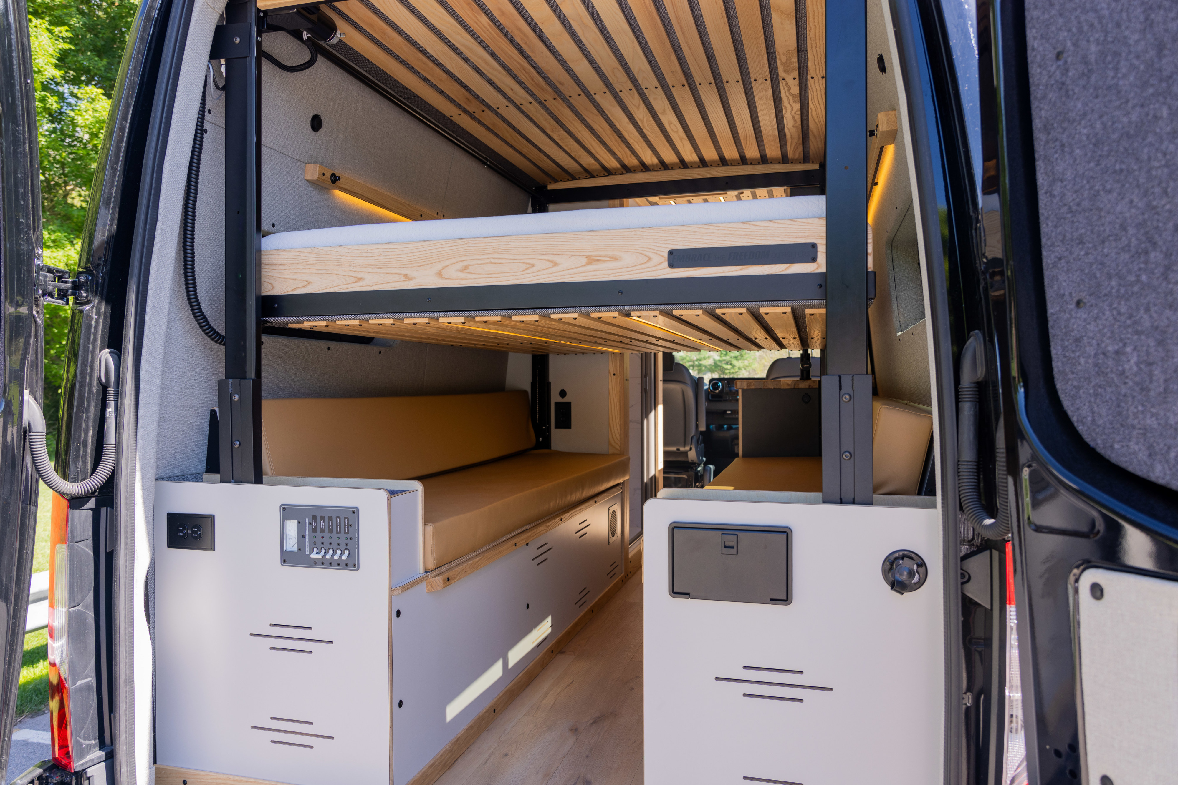 Modern rv rental camper van interior featuring comfortable bunk beds, tan cushions, and a control panel.. Mercedes Sprinter 2022