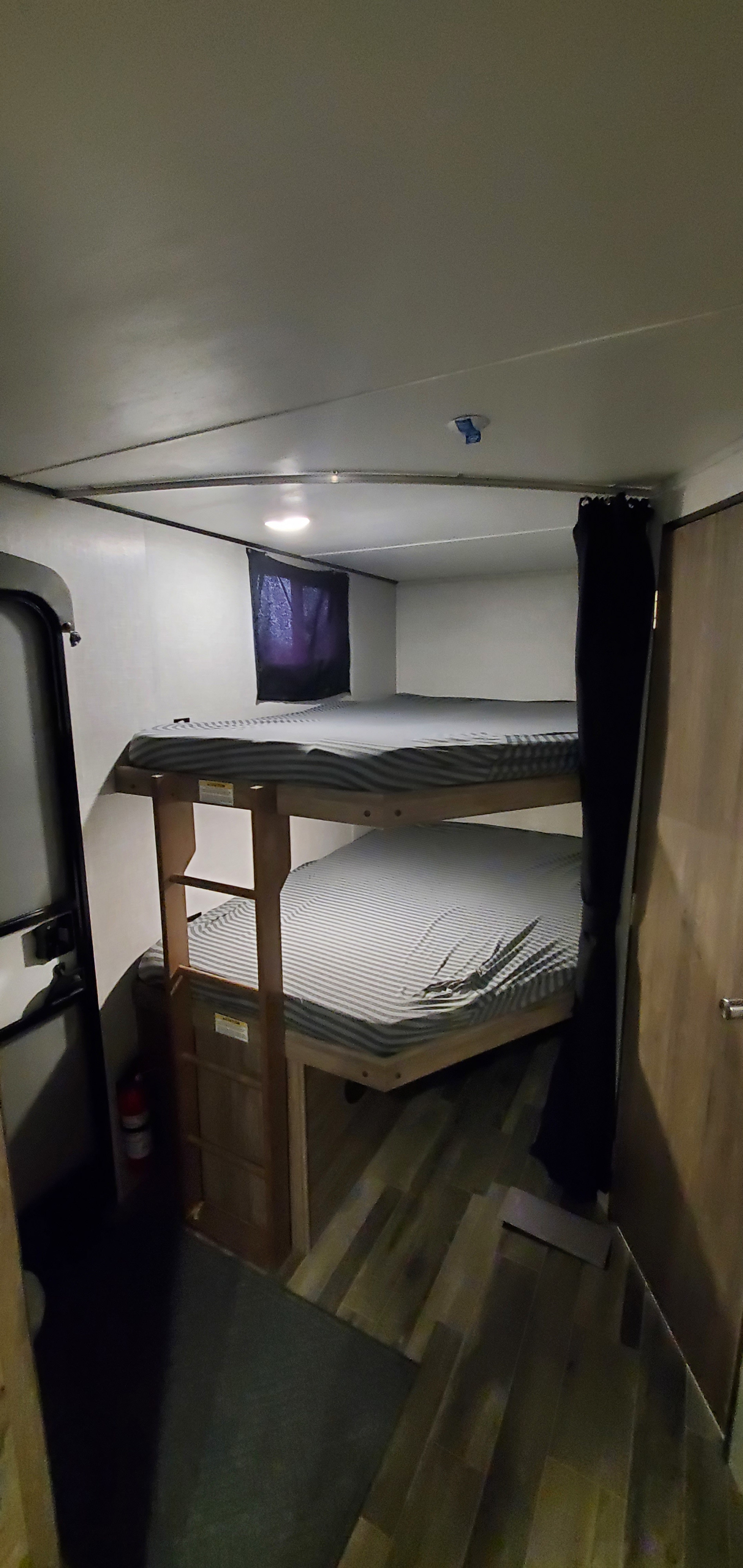 This RV rental interior features compact bunk beds with striped mattresses, a privacy curtain, and a fire extinguisher.. Keystone RV ZR280BH22 2022