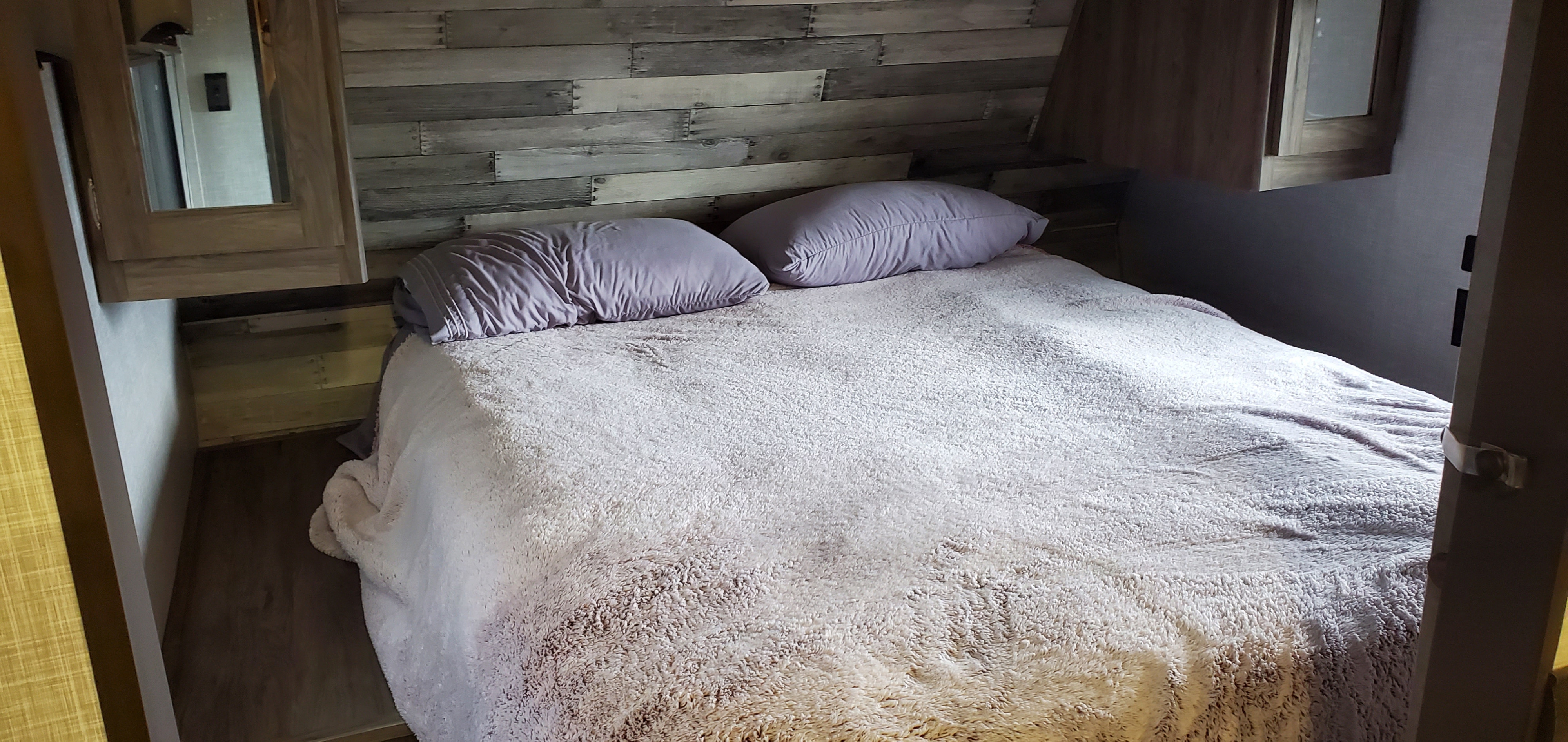 Cozy RV rental bedroom featuring a comfy bed with a fluffy blanket, purple pillows, and a rustic wood-paneled wall.. Keystone RV ZR280BH22 2022