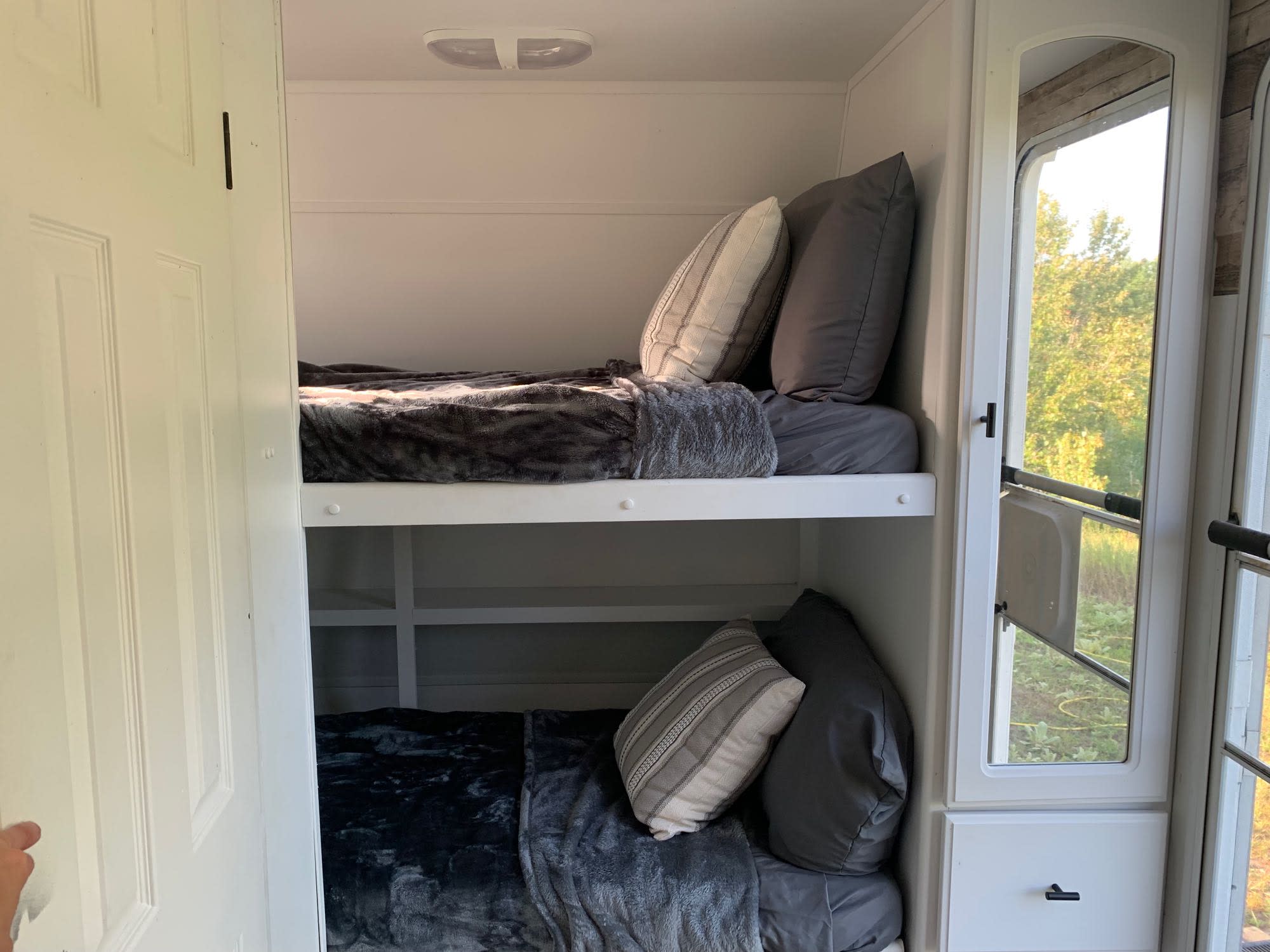 Cozy RV rental interior featuring comfortable bunk beds with soft bedding. A window offers a bright view of nature.. Lite Way Outback 2003