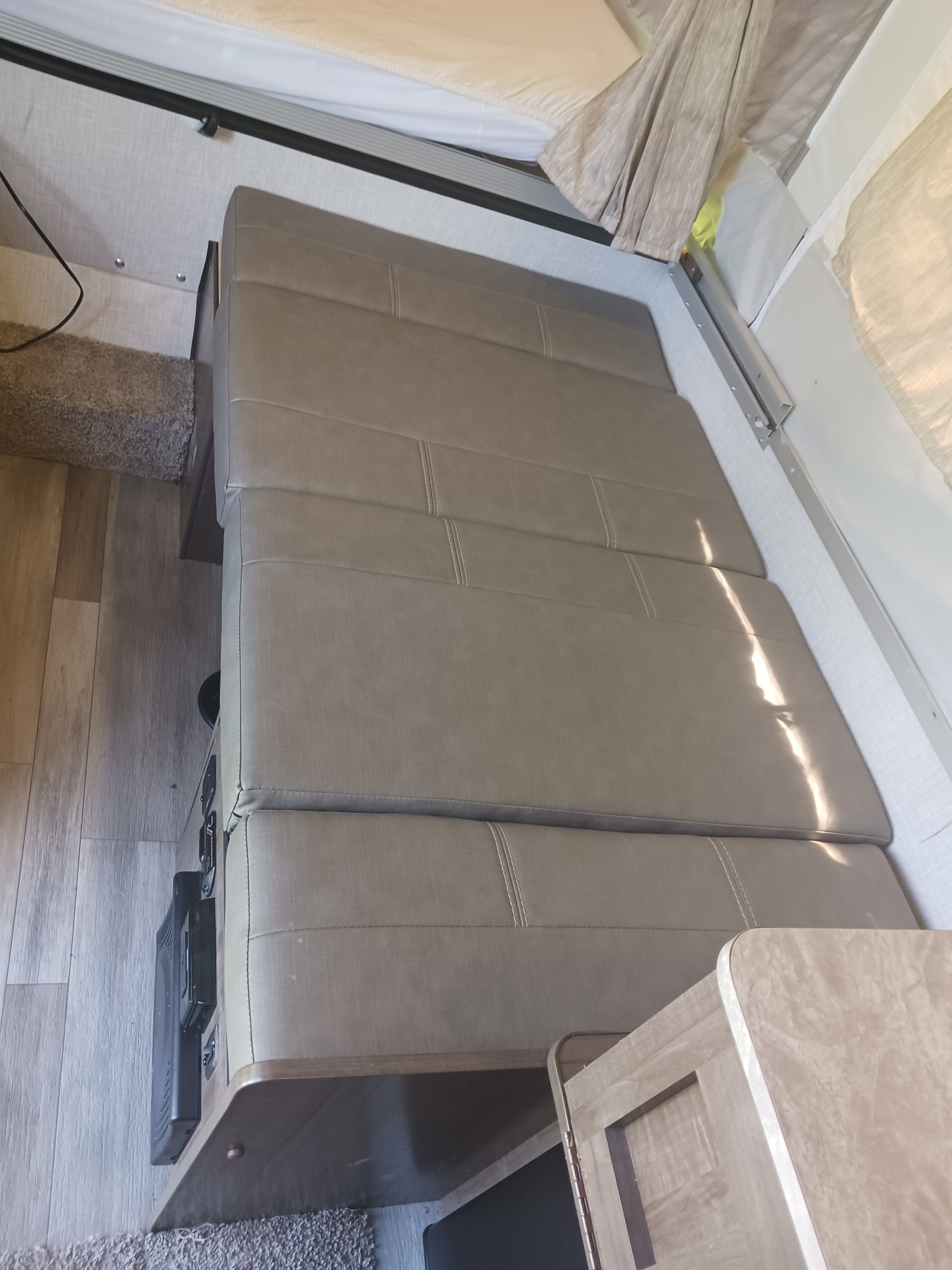 Comfortable dinette/sofa area inside an RV rental, featuring plush seating, wood-look flooring, and a sleeping bunk above.. Forest River Rockwood Freedom 2022