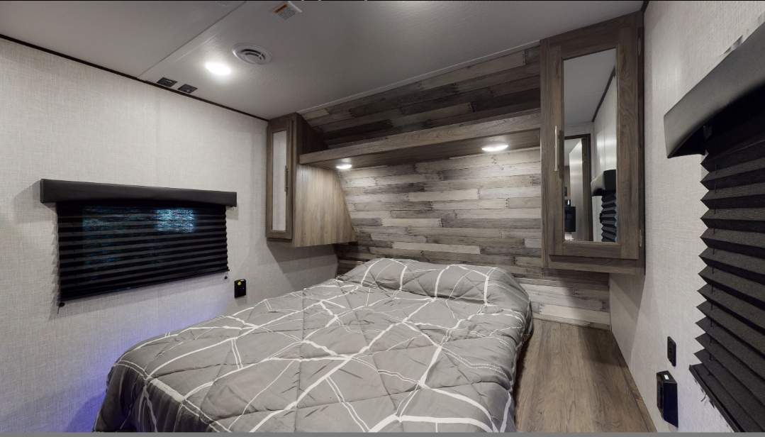 RV rental bedroom: a compact space with a grey bed, wood plank accent wall, overhead cabinets, and dark window blinds.. Crossroads RV Zinger 2020