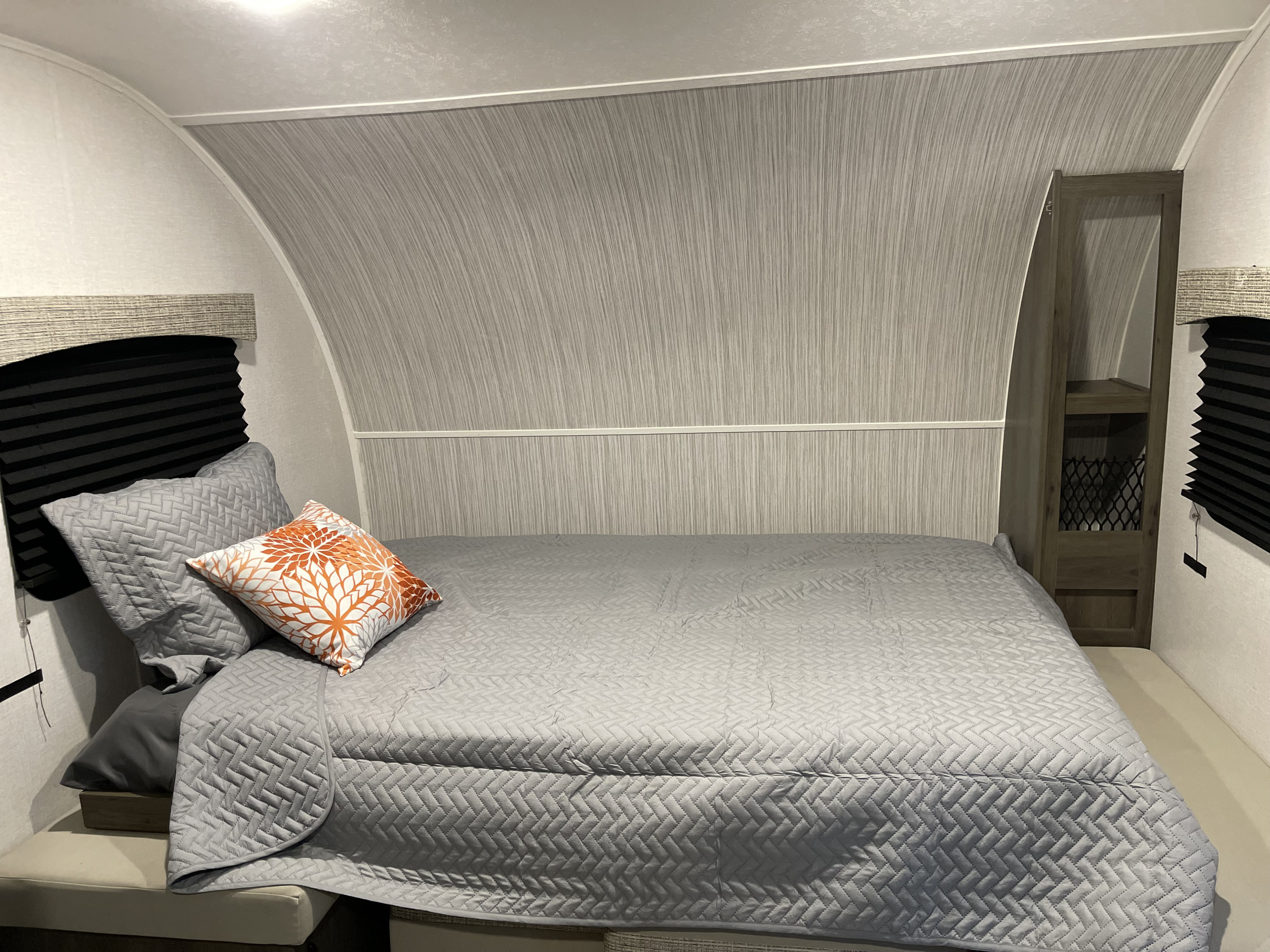 Cozy RV rental bedroom with grey quilted bedding, an orange accent pillow, and built-in storage. Ideal for travel.. Coachmen Viking 162RBU 2022