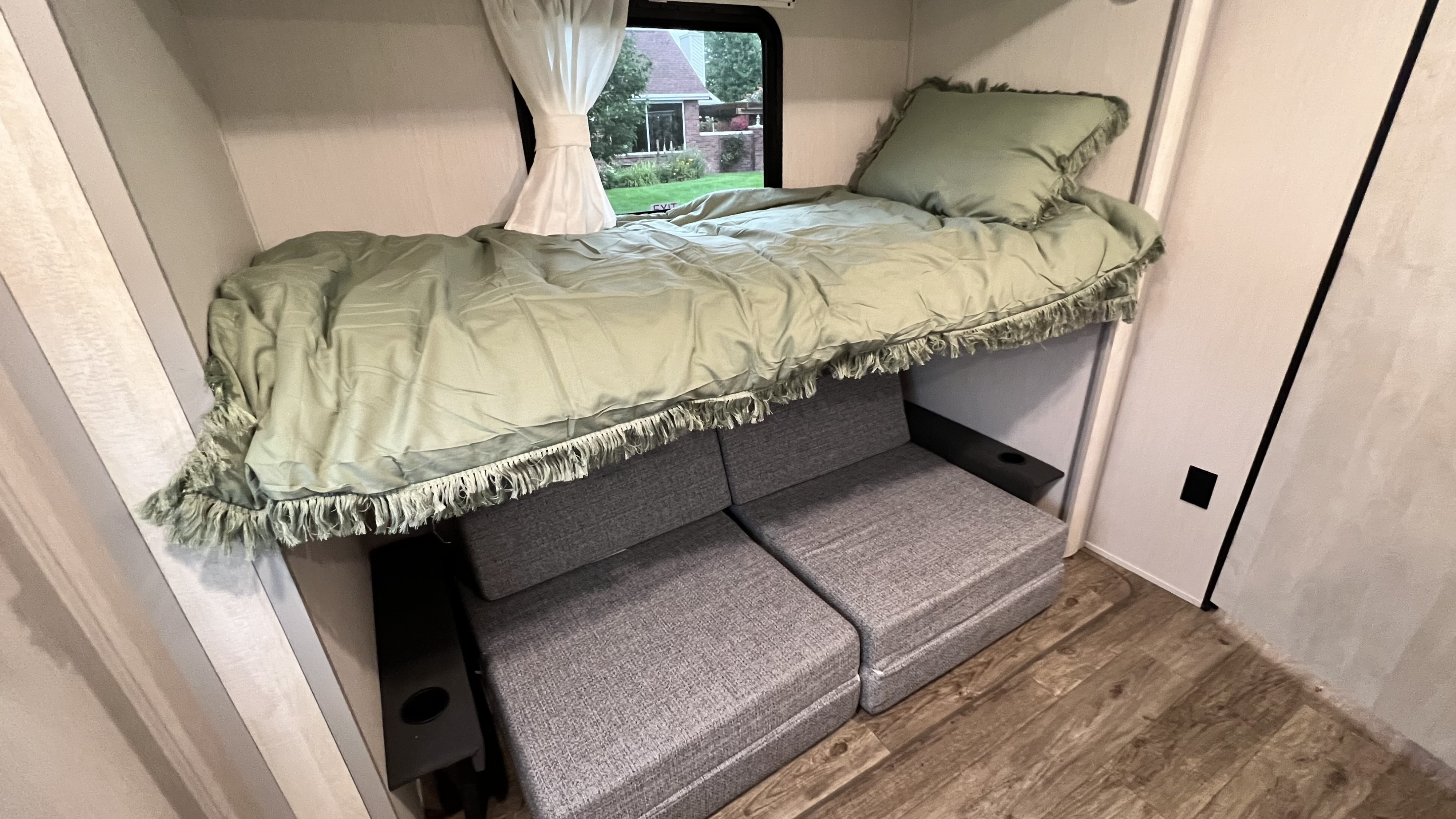 Cozy RV rental bunk bed with soft green bedding over versatile gray seating. A compact, comfy travel space.. Forest River Vibe 2023