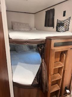 Inside an **RV rental**: view of twin **bunk beds** with white bedding, curtains, and convenient built-in storage shelves.. Jayco Jay Flight 2017