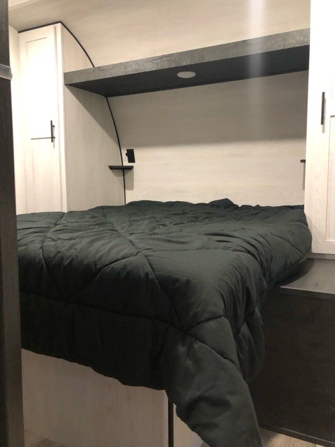 RV rental: Modern and cozy bedroom featuring a dark green bed, white storage cabinets, and an overhead shelf with integrated lighting.. KZ 301 2023