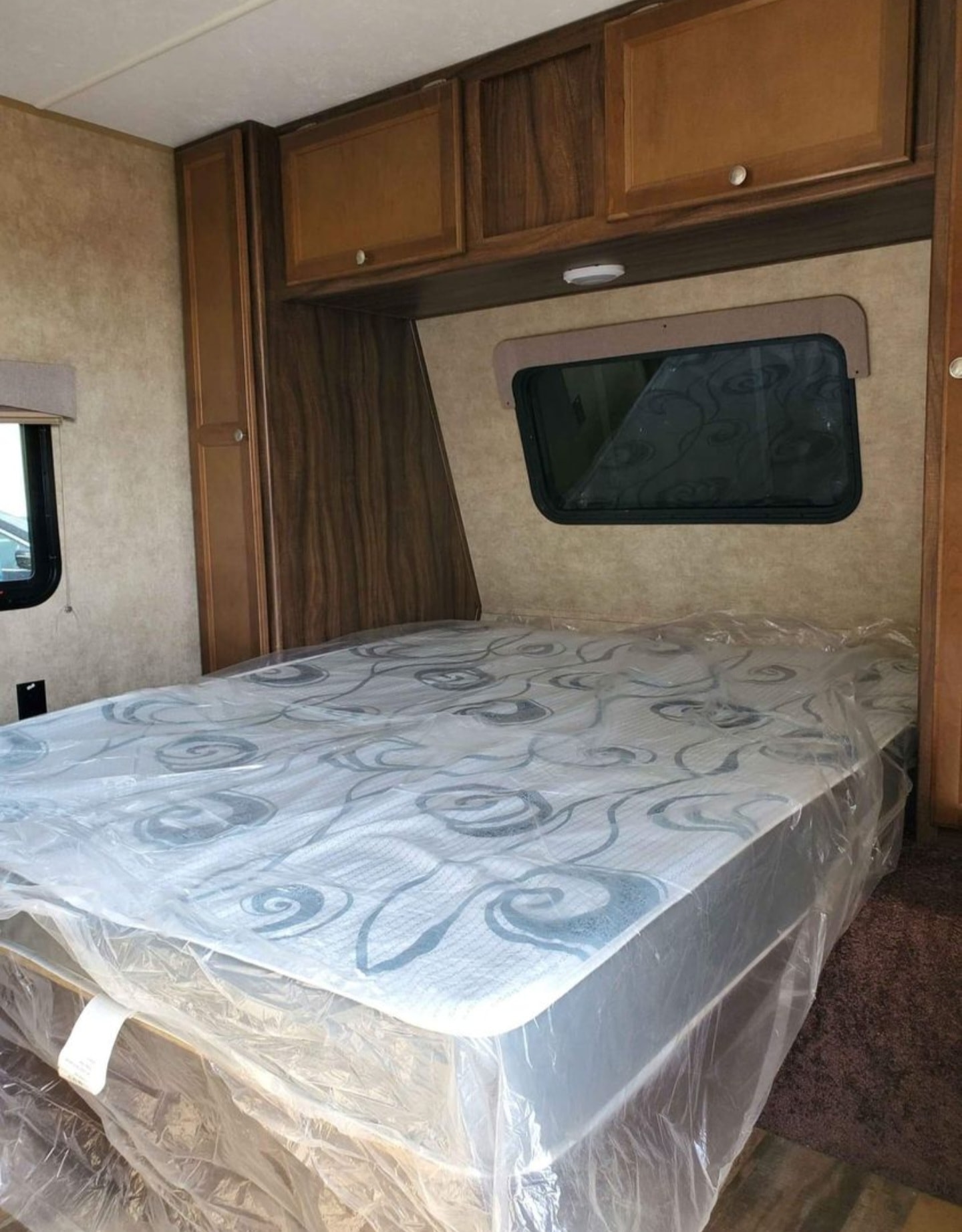 Inside an RV rental bedroom: a fresh mattress in plastic, compact cabinets, and a window. Ready for cozy travel.. Viking 21RD 2019
