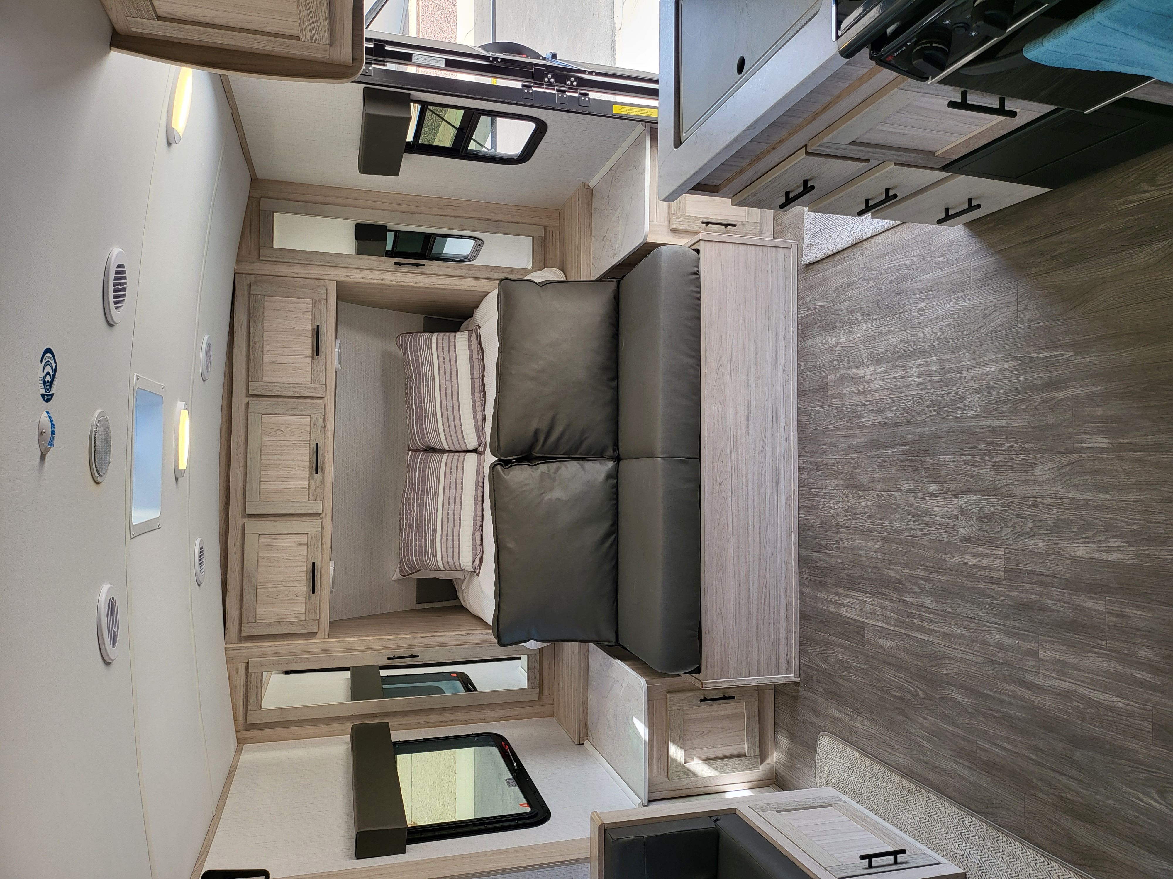 Inside this modern RV rental: a flexible lounge and sleeping area with sleek cabinetry, kitchen, and wood-look flooring.. Cruiser RV Twilight Adventure 210 2022