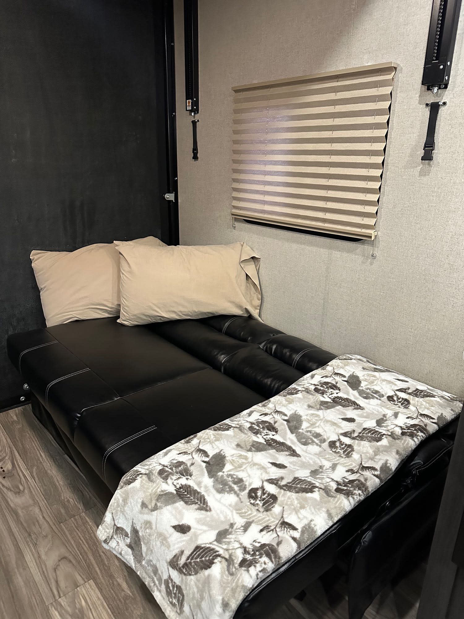 Inside this RV rental: a plush black sofa bed, complete with beige pillows and a decorative throw blanket, set on wood flooring.. Genesis Supreme Wanderer 2021