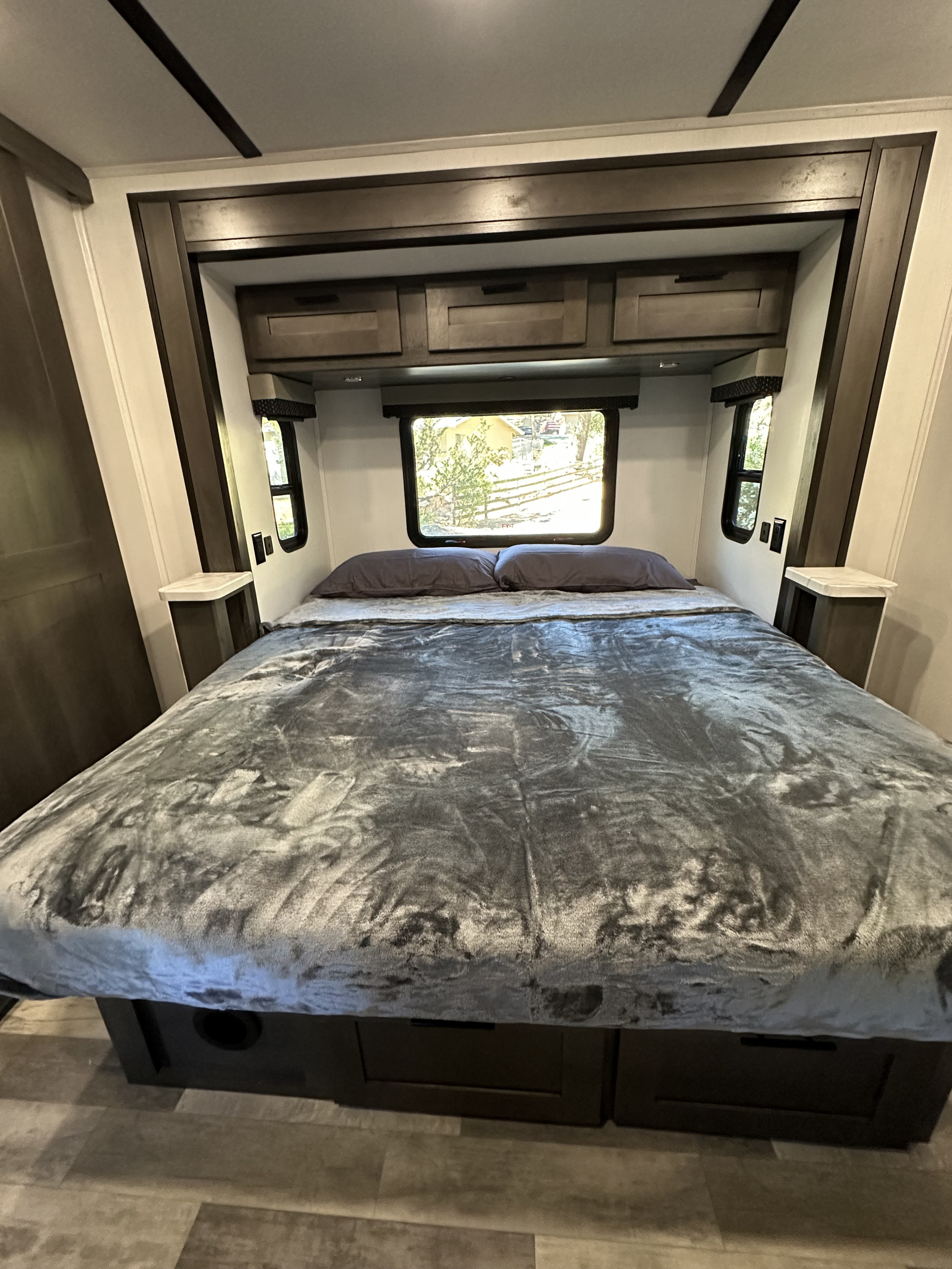Cozy RV rental bedroom with a plush bed, overhead cabinets, and windows offering outdoor views. Relax on your trip!. FR3 FR3 Motorhome 2023