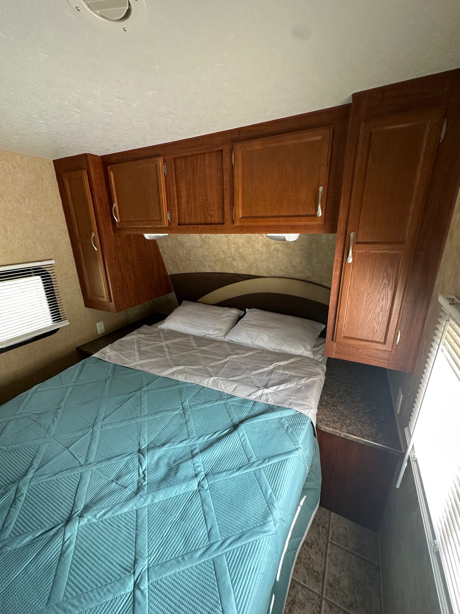 Cozy RV rental bedroom with a neatly made bed, overhead wood cabinets, and windows. Perfect for travel!. Jayco Jay Flight 2010