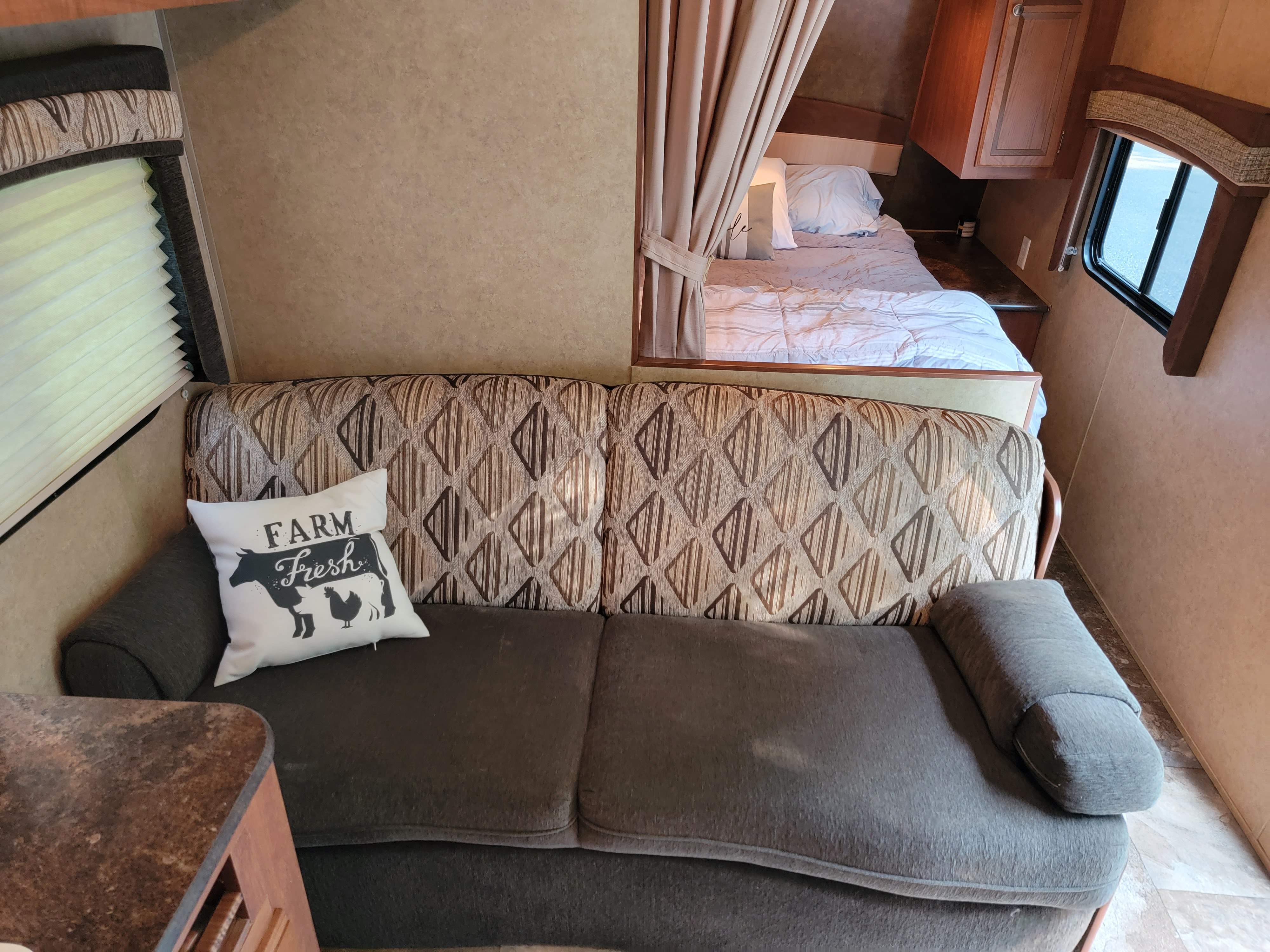 Cozy RV rental interior: sofa, "Farm Fresh" pillow, and bed area. Perfect for travel.. Jayco Jay Flight 2013