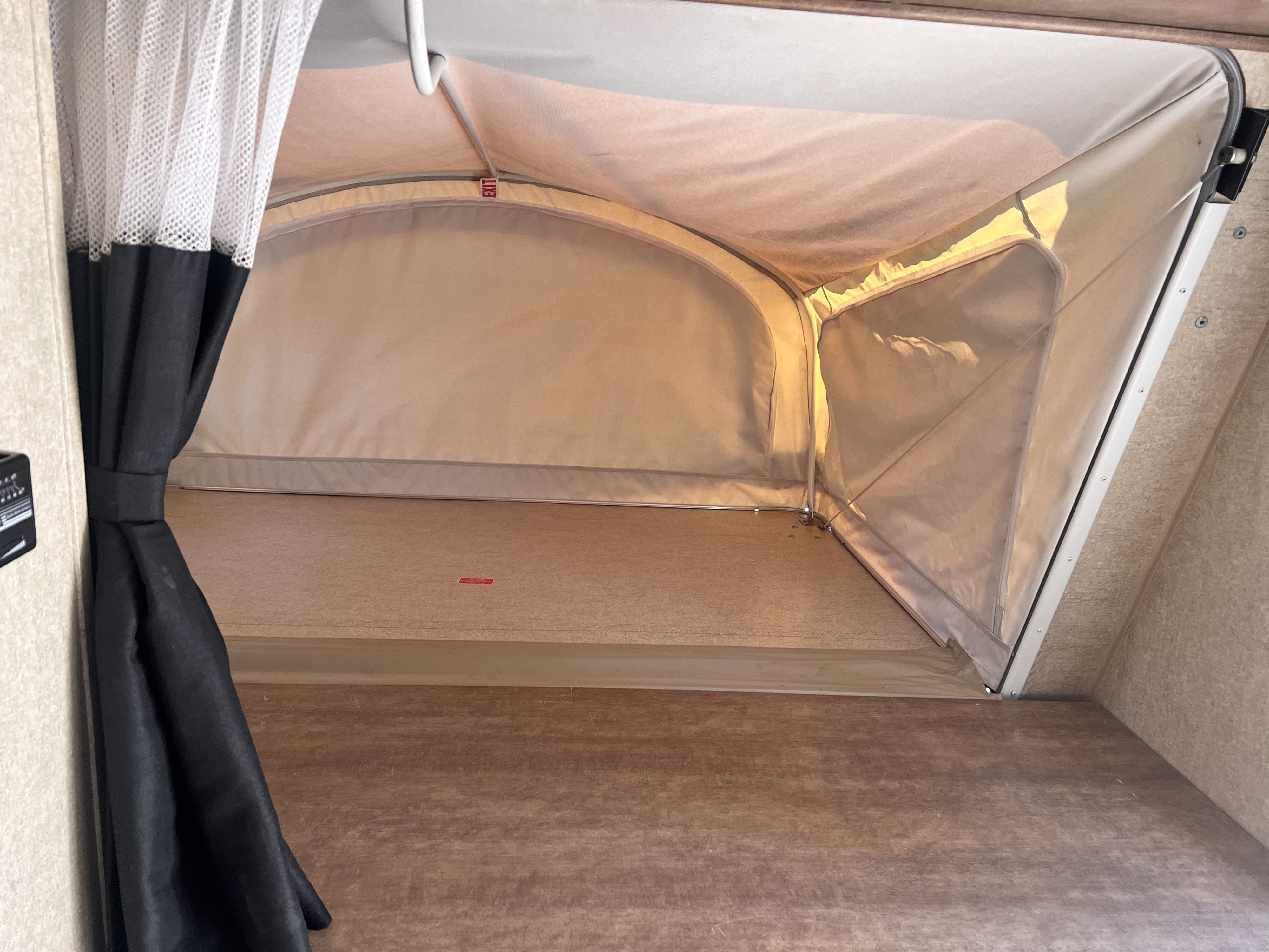 Interior of an rv rental's pop-out tent bed area, featuring light fabric walls, wooden platform, and mesh curtain.. Starcraft Satellite 2018
