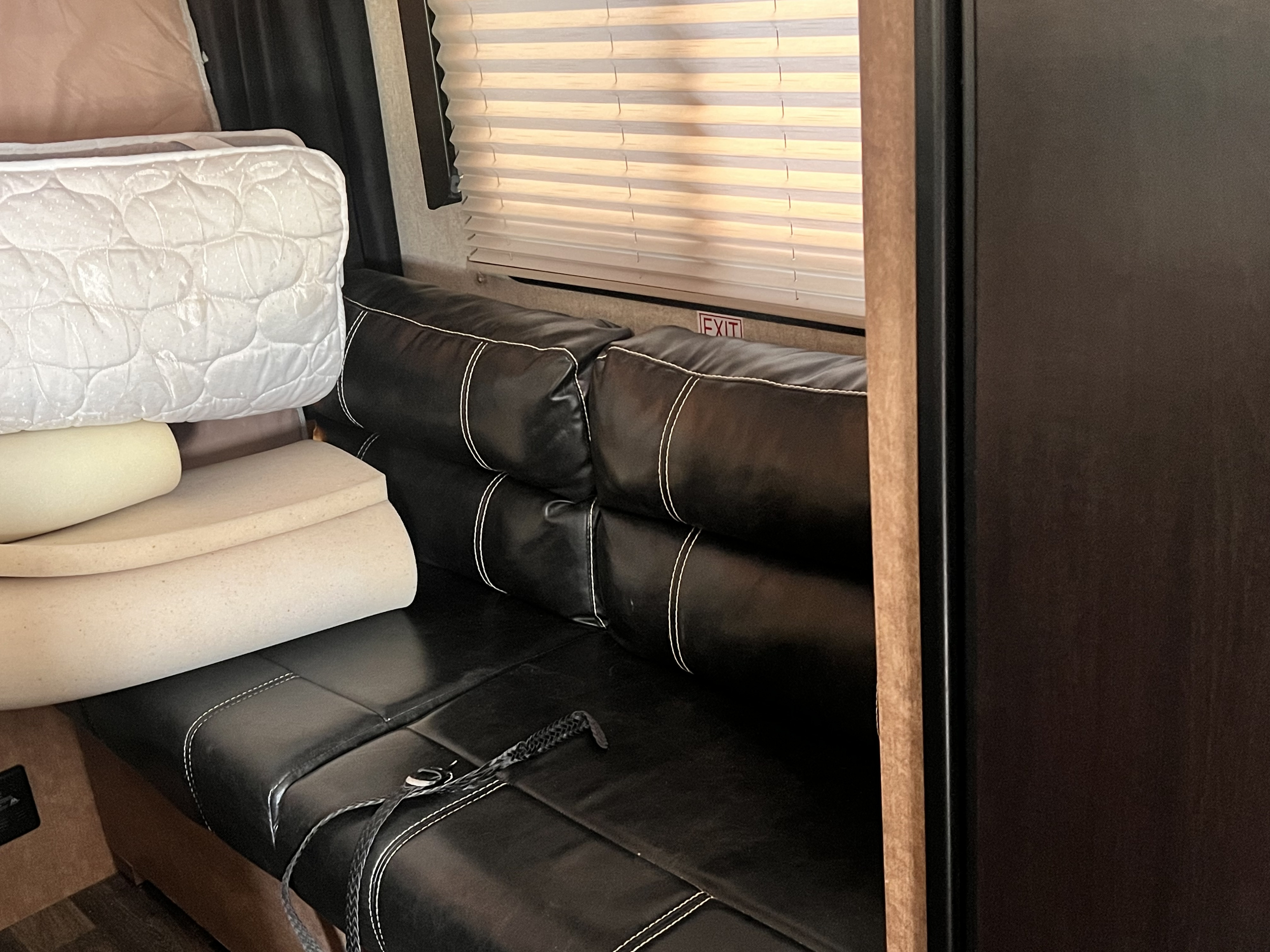 RV rental interior: Black faux leather convertible couch with stacked cushions for a bed, window blinds, and an 'EXIT' sign.. Starcraft Satellite 2018