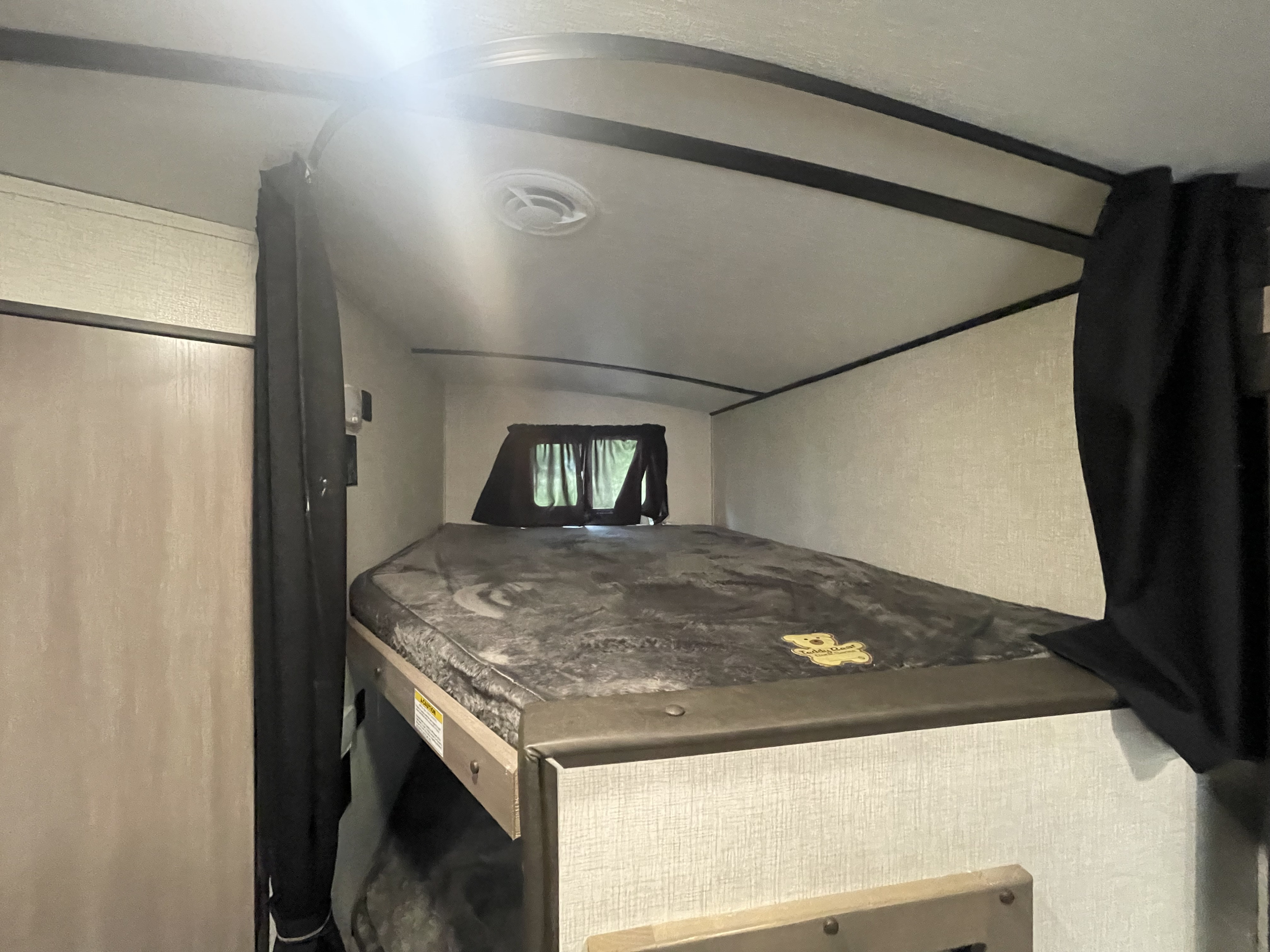 RV rental interior shows a cozy bunk bed with grey blanket, window, and ceiling vent, offering comfortable travel.. Crossroads RV Sunset Trail 2022