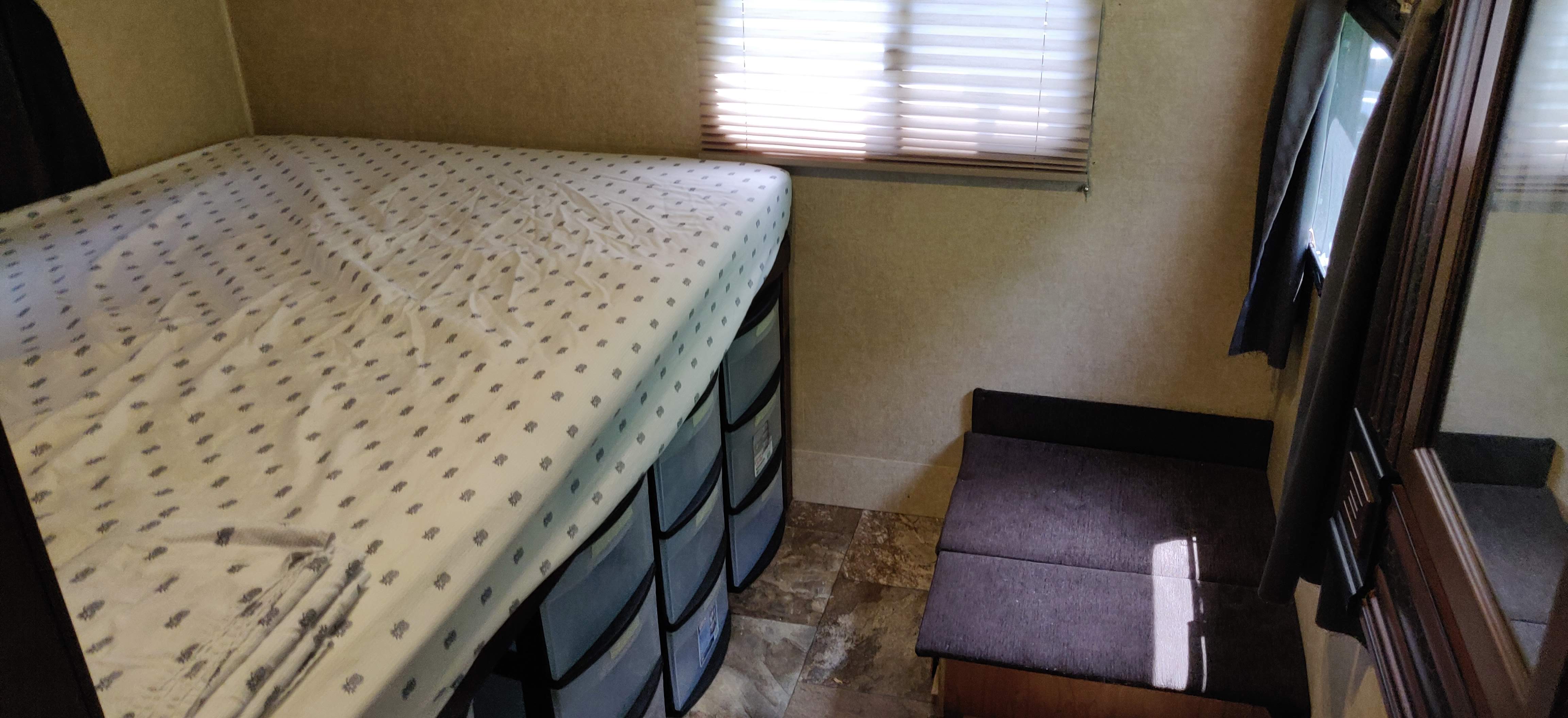 Compact RV rental bedroom showing an elevated bed, under-bed storage drawers, window with blinds, and small seating.. Jayco White Hawk Ultra Lite 2014