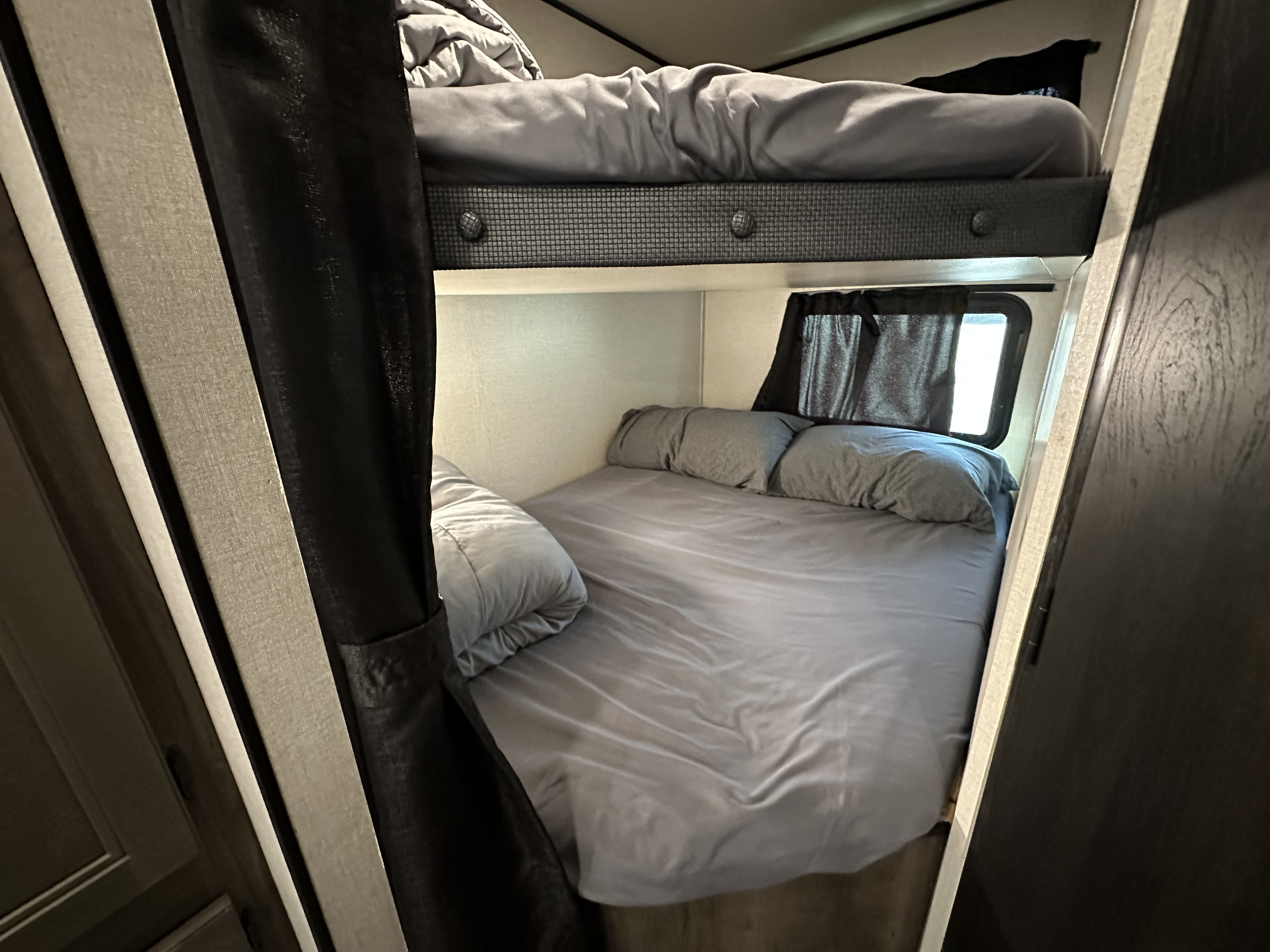 Cozy gray bunk beds in an RV rental, offering a comfortable sleeping area with curtains and windows.. Starcraft Autumn Ridge 2022