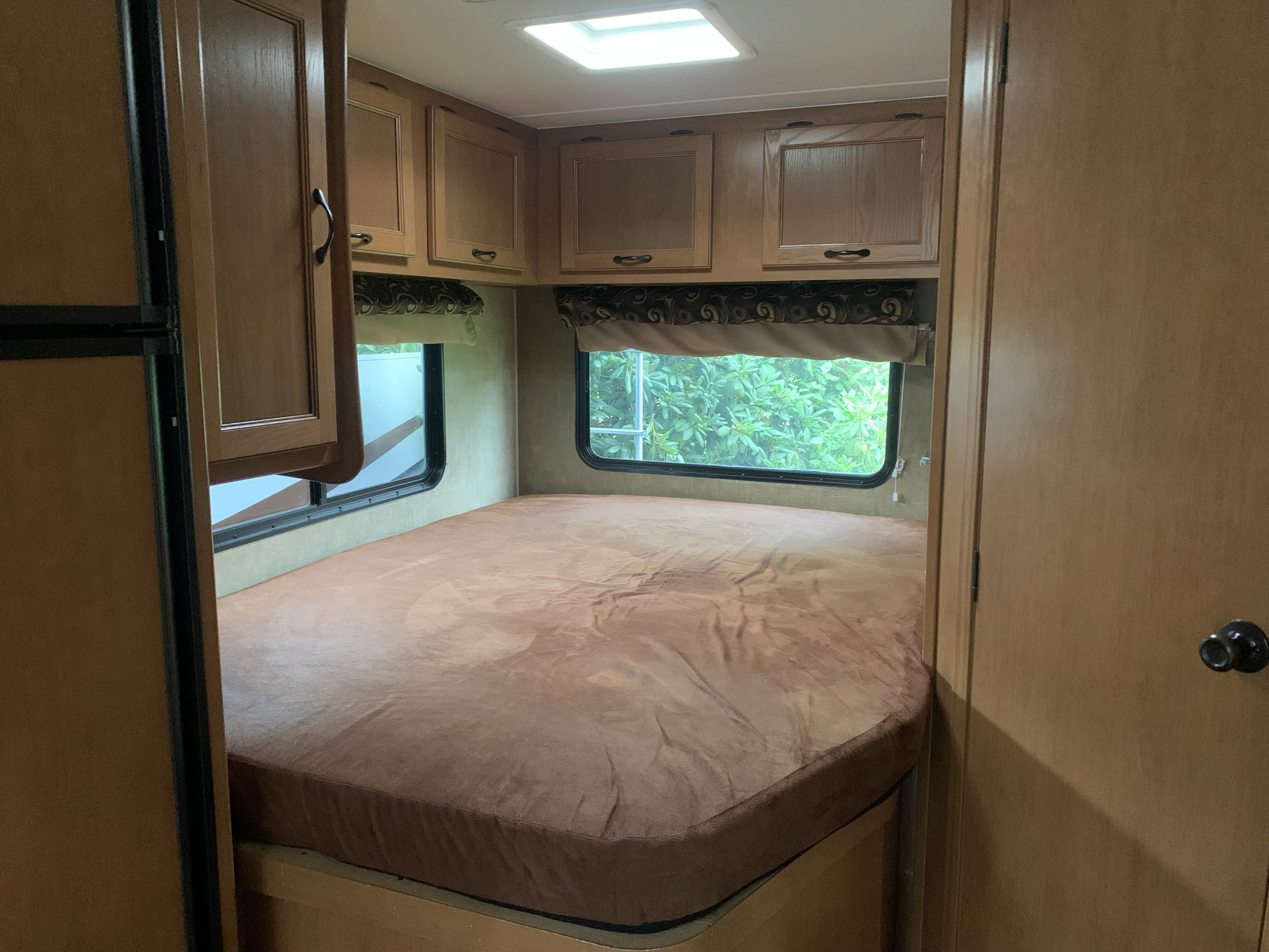 Cozy RV rental bedroom featuring a large bed, overhead storage cabinets, and nature views from the windows.. Other Other 2014