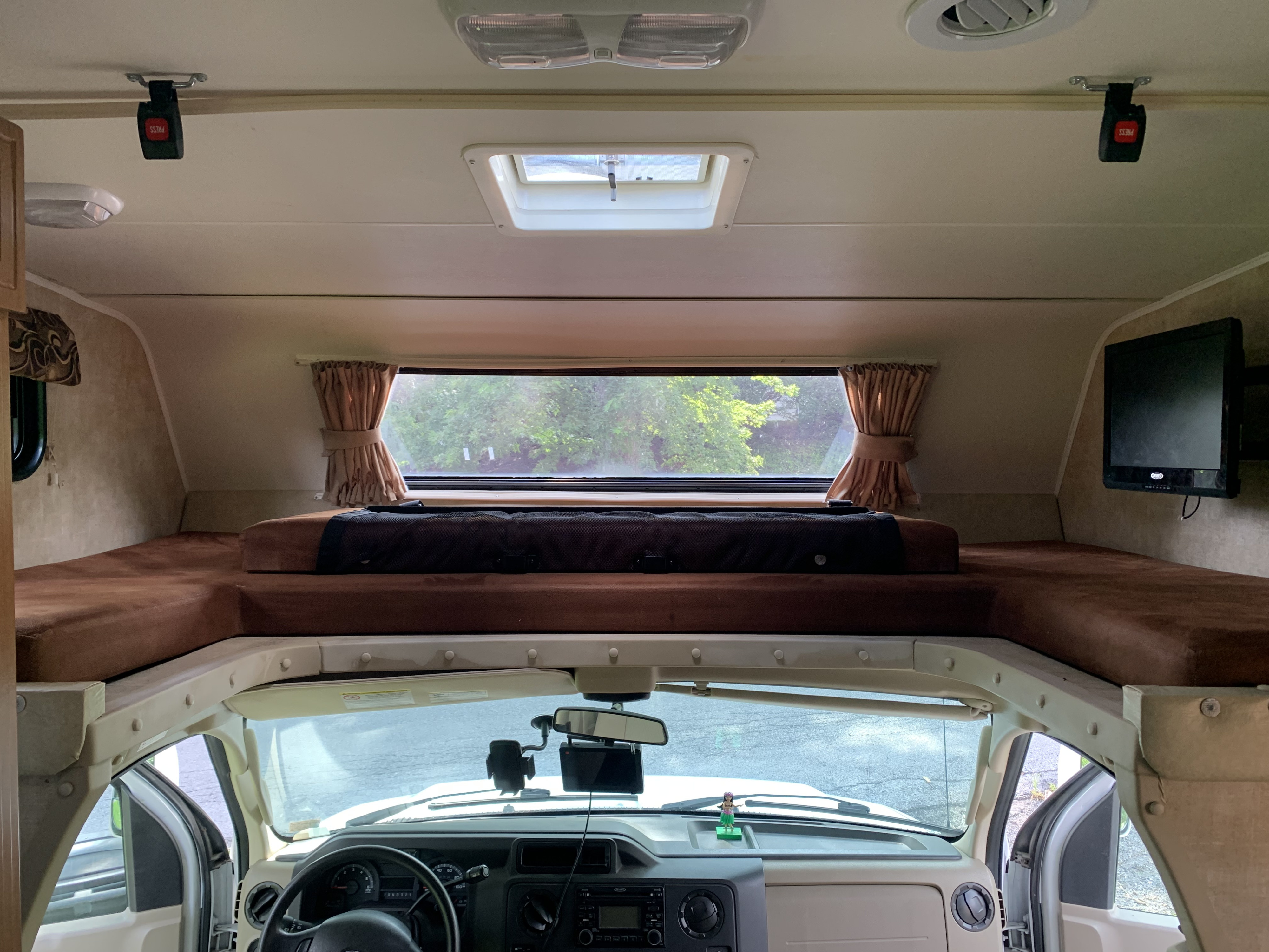 Interior of an RV rental, looking towards the cab-over bunk with a safety net, window, and wall-mounted TV.. Other Other 2014