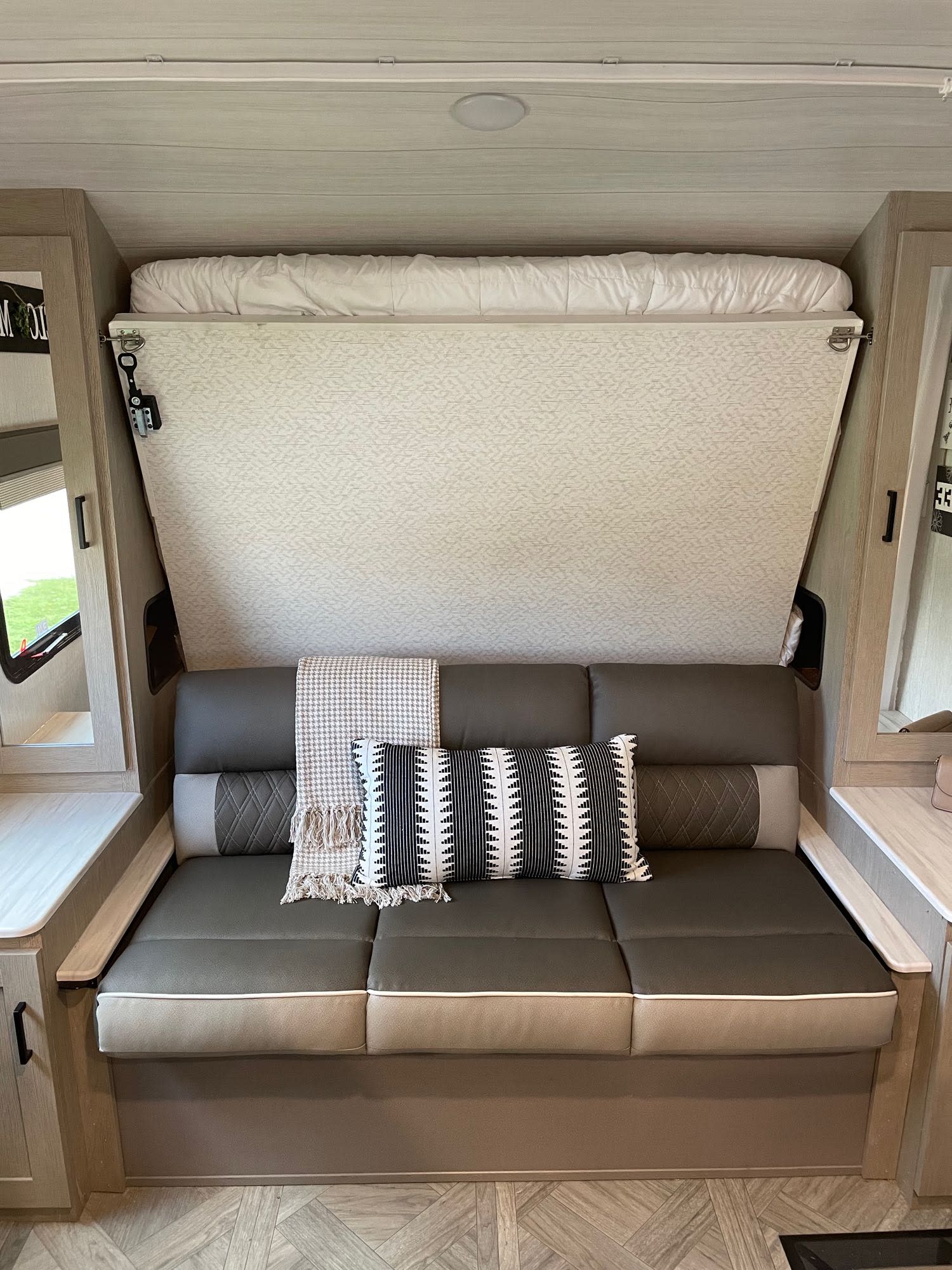 RV rental interior: A gray sofa with pillows and blanket sits beneath a folded-up bed, maximizing compact living space.. Forest River Salem Cruise Lite Platinum 2023