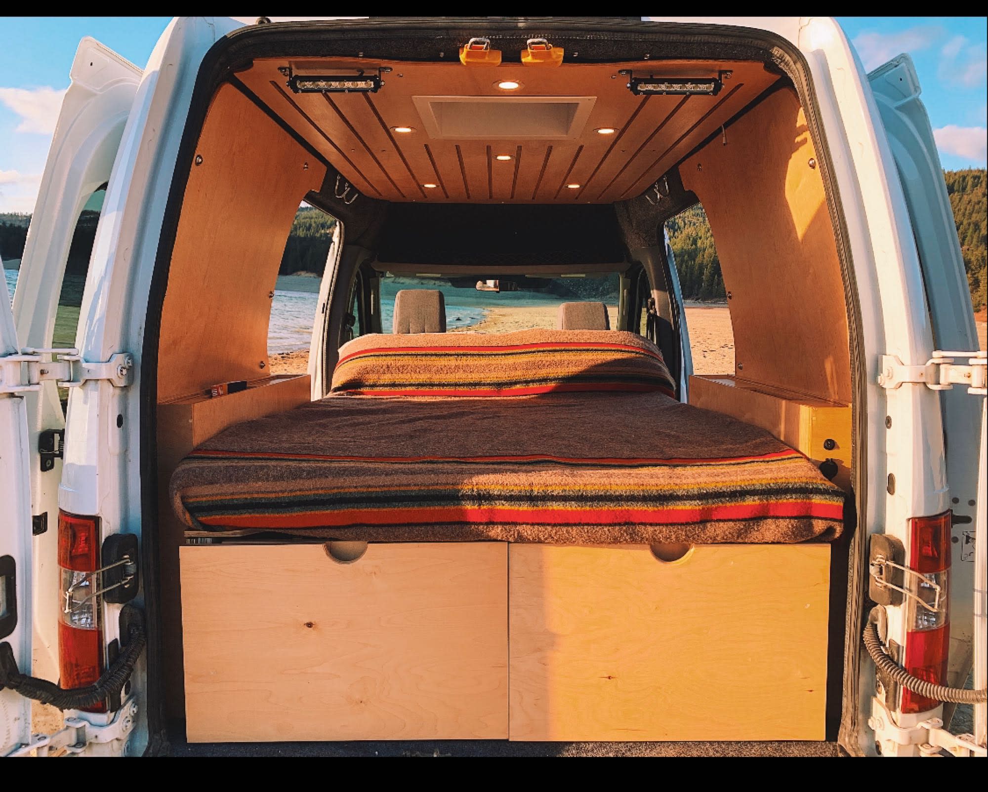Cozy RV rental campervan interior: bed, storage, wood paneling, and an inviting lake/forest view for epic road trips.. Ford Transit Connect 2010