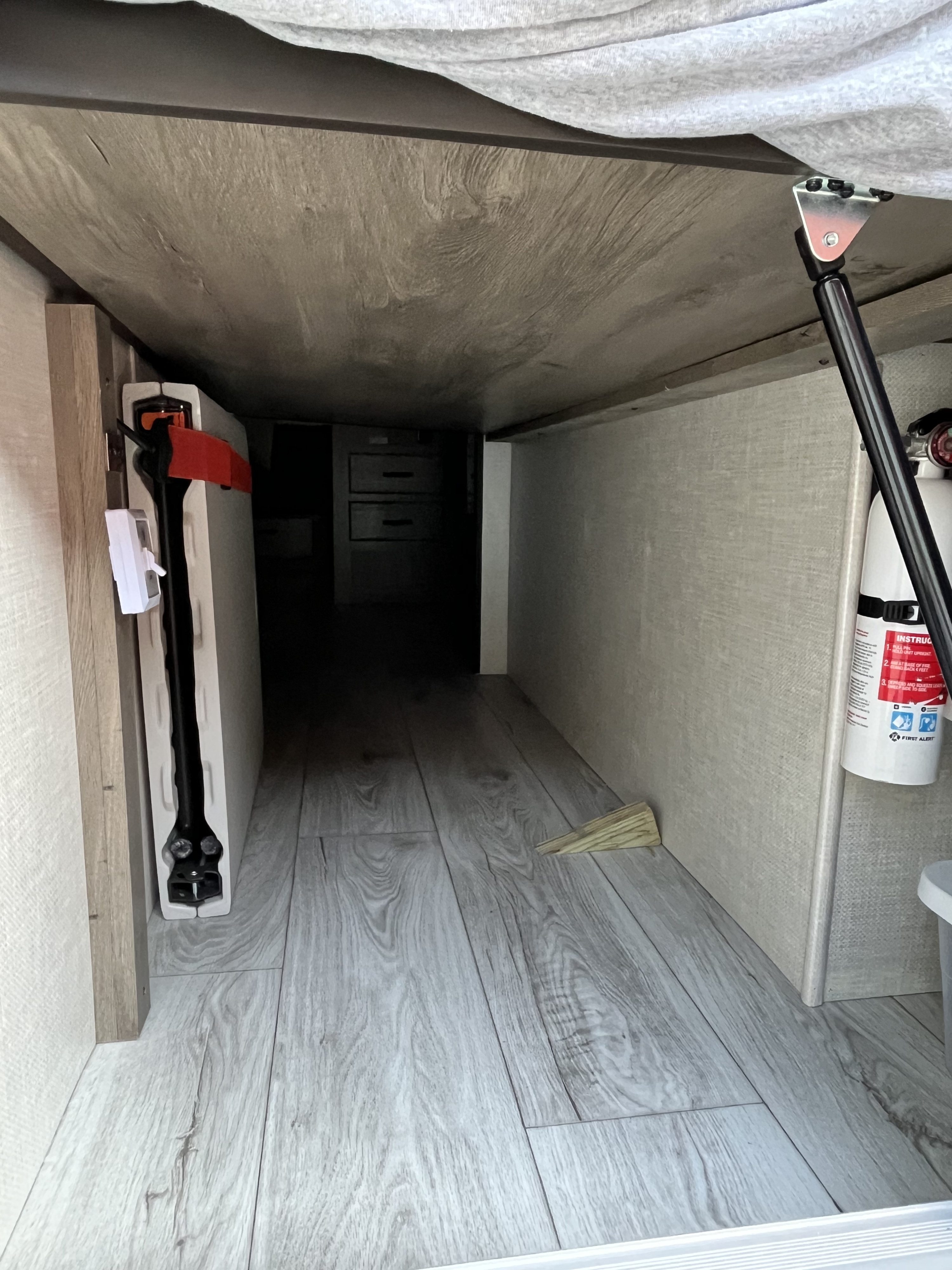 Under-bed storage area in an RV rental, featuring laminate flooring, a fire extinguisher, and a stored folding chair.. Forest River Surveyor Legend 2022