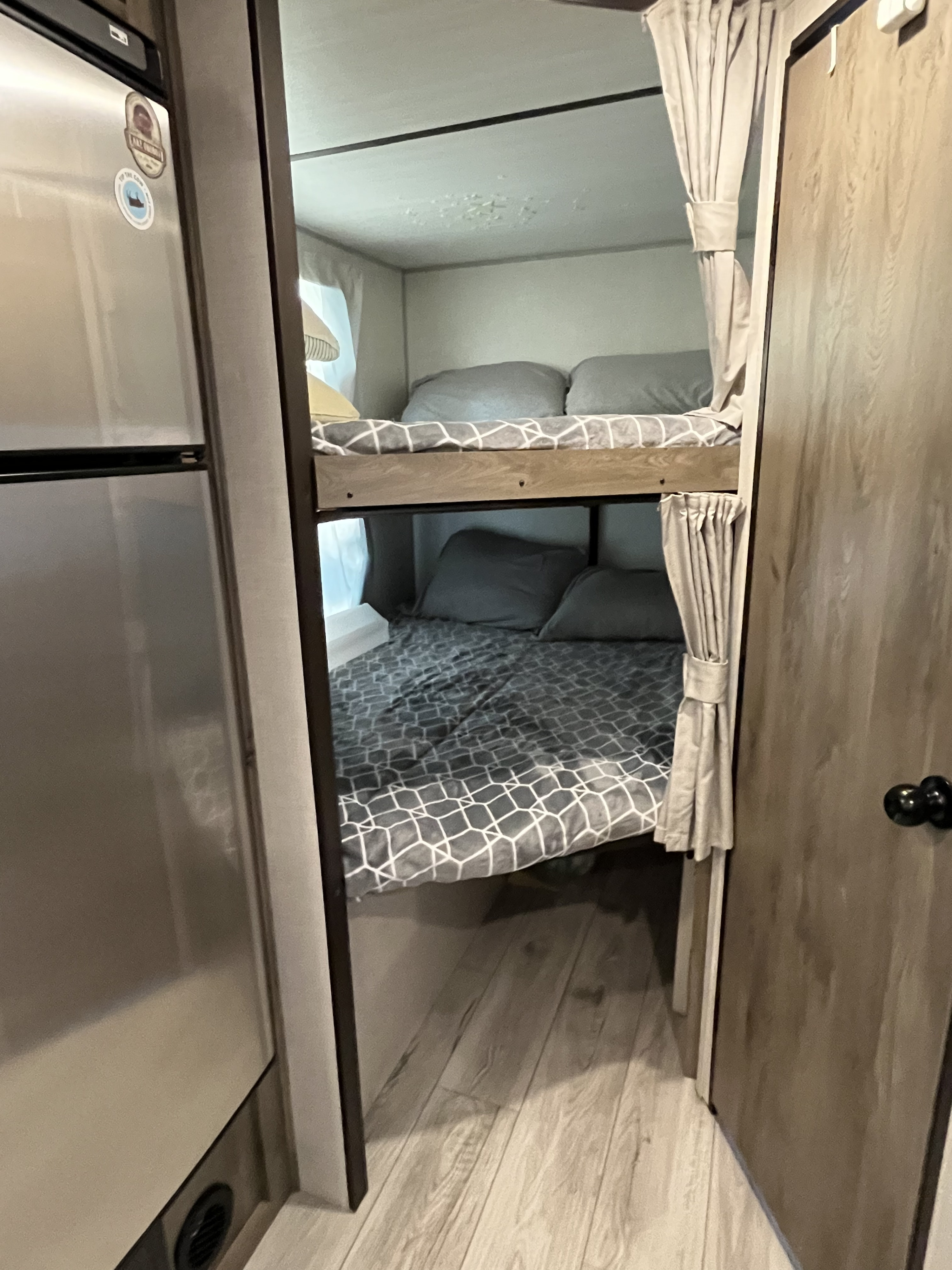 Cozy RV rental interior showcasing comfortable bunk beds with gray bedding, next to a stainless steel refrigerator.. Forest River Surveyor Legend 2022