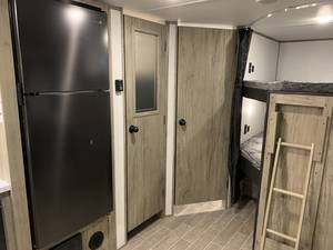 RV rental interior: full-size fridge, compact storage doors, and cozy bunk beds with a ladder. Ideal for family travel.. Forest River Cherokee Alpha Wolf 2022