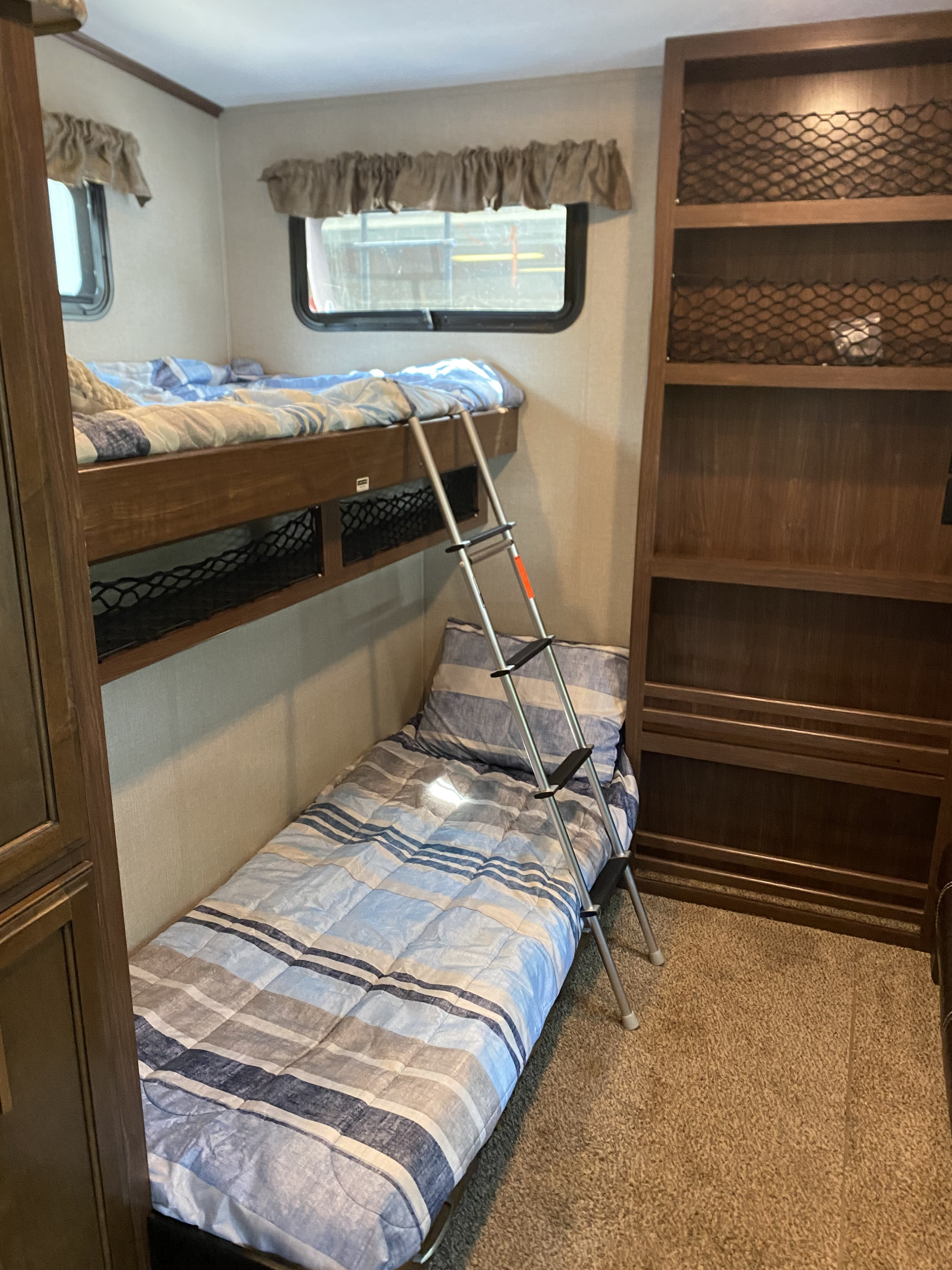 Inside this RV rental: a comfortable bunk bed setup with striped bedding, ladder, and convenient built-in storage shelves.. Keystone RV Montana High Country 2017